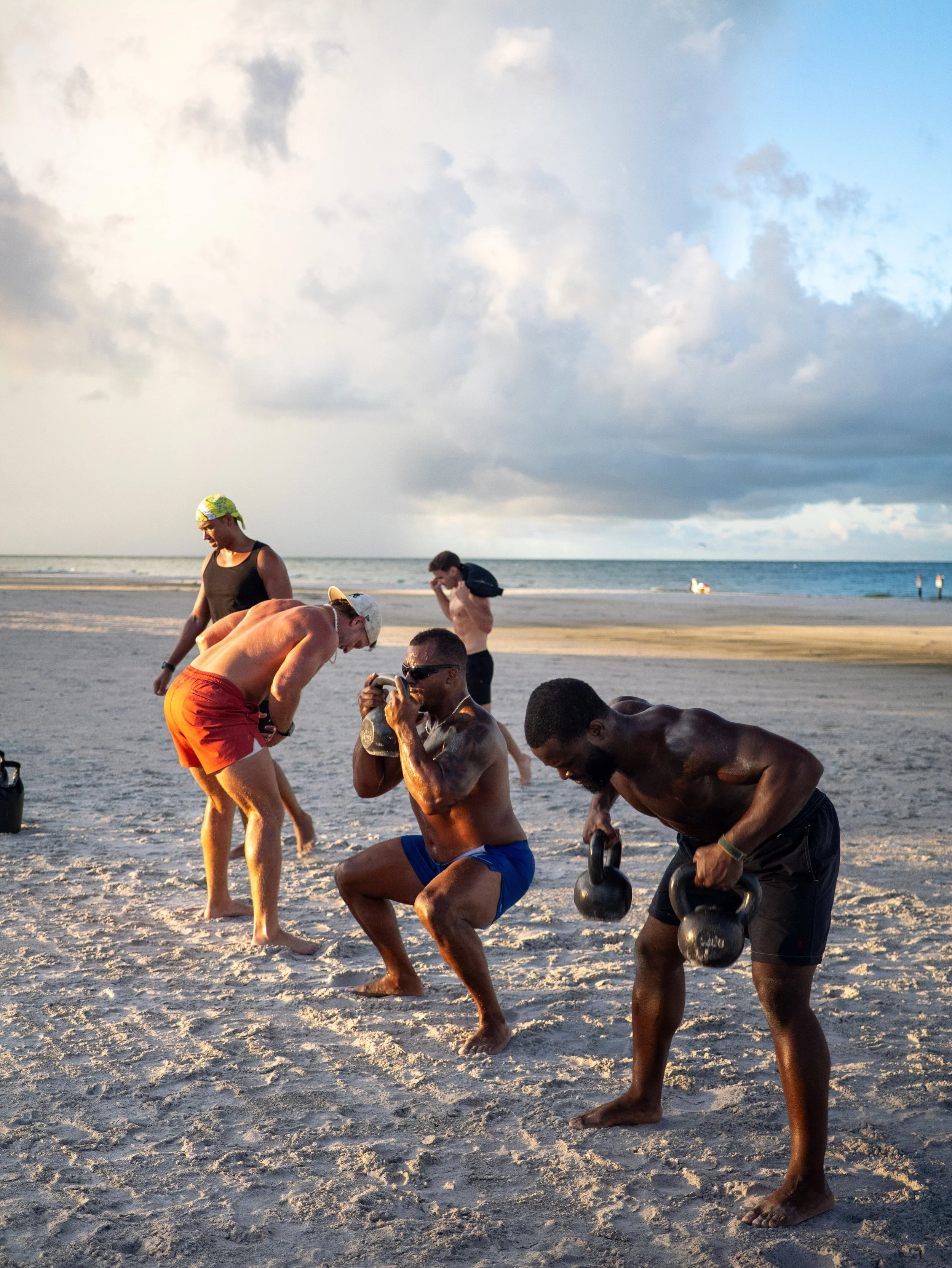 A group of men participating in a LUVSUM outdoor functional fitness workout on the beach.