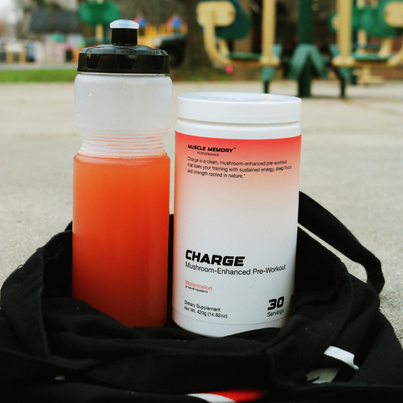 Sports bottle of prepared watermelon CHARGE pre-workout beside a CHARGE bottle and gym bag