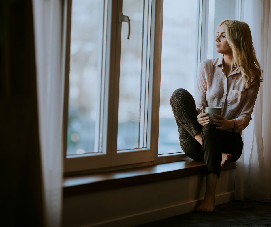 Woman sitting by window reflecting while starting her fertility journey