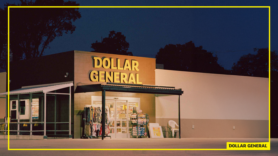 A Dollar General store at night with brightly lit yellow sign, showing outdoor display racks of clothing, snacks, and a plastic chair near the entrance.