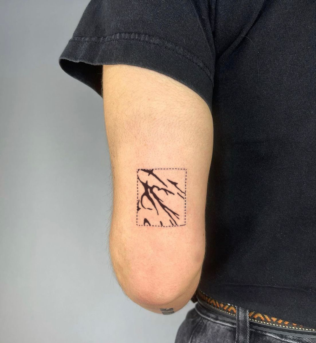 Tattoo of a mountain scene with trees on the inner bicep of a person's arm, with a dotted square outline.