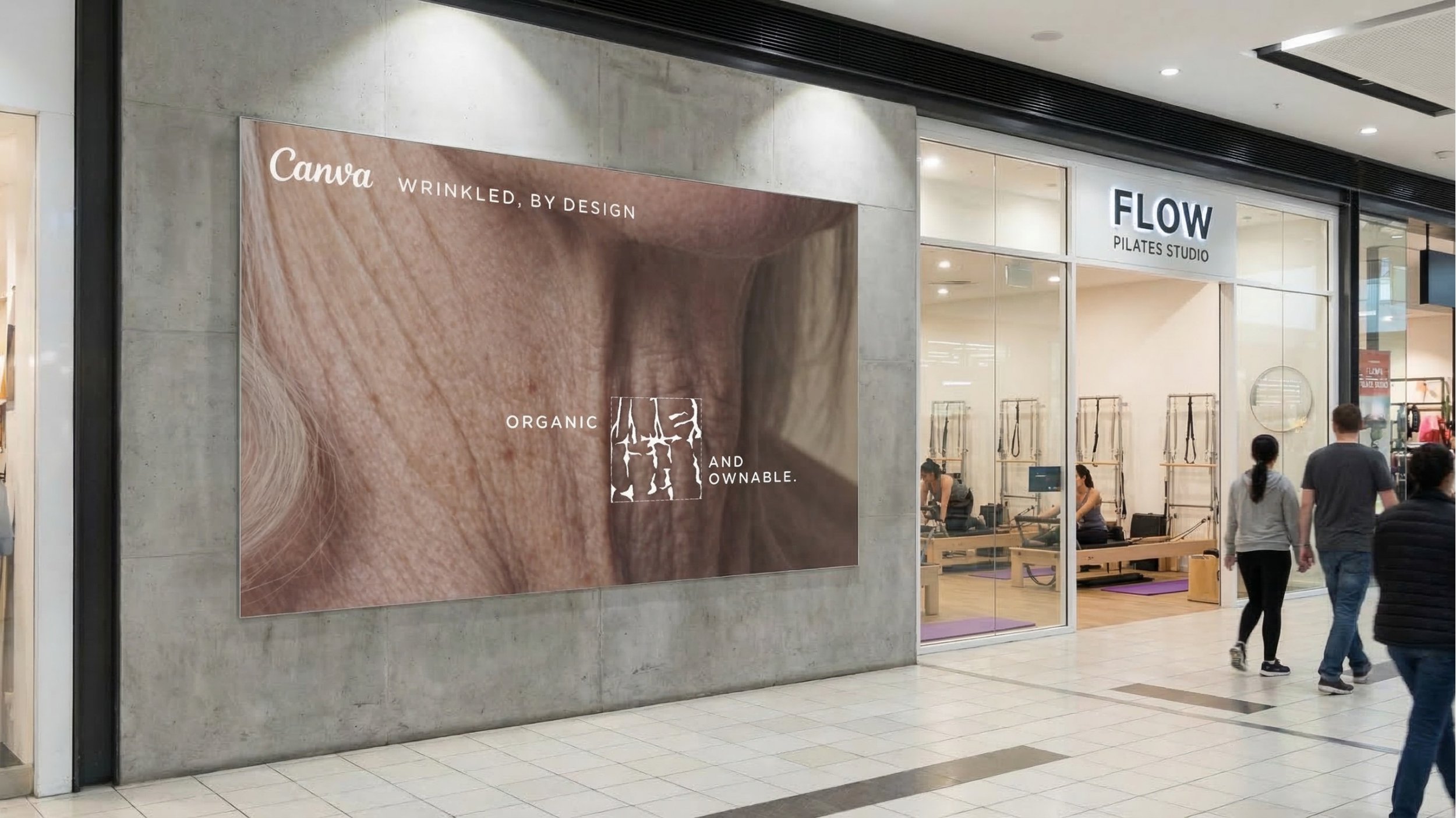 Large advertisement on a concrete wall featuring a close-up of wrinkled human skin with text promoting organic, age-aware skincare products. To the right, a Pilates studio with glass walls and signs is visible, with people walking past in a shopping mall.