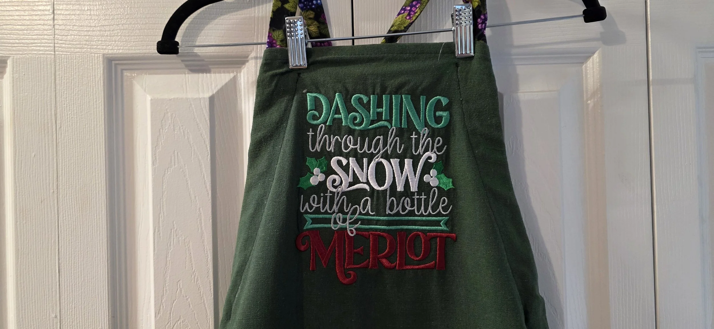 Adjustable green embroidered tea towel apron with grape cloth pocket.
