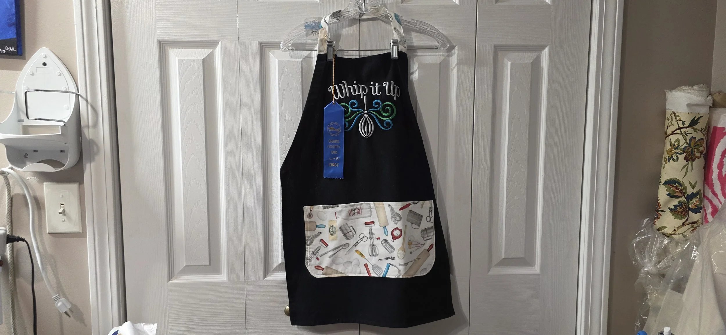 Adjustable black embroidered tea towel apron with kitchen cloth pocket.