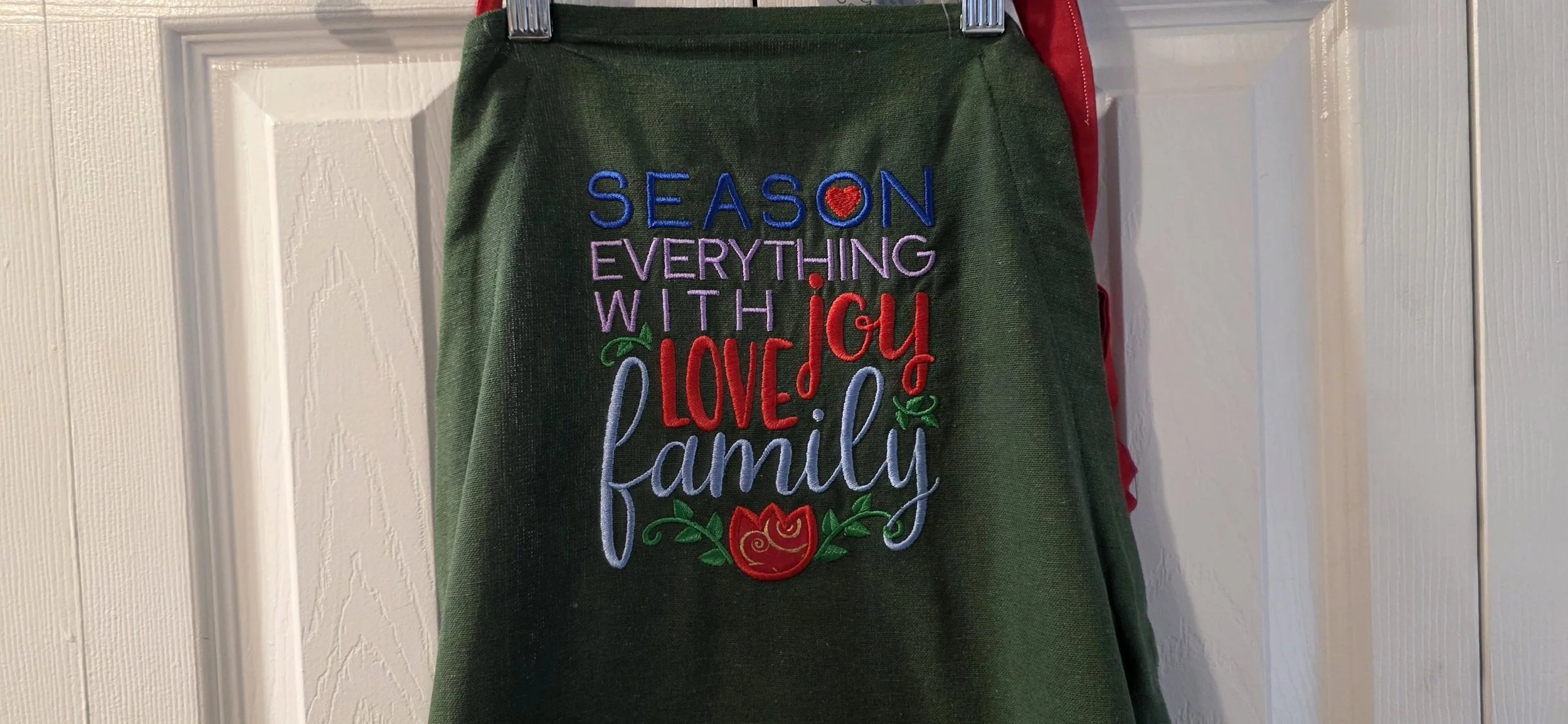 Adjustable green embroided tea towel apron with apple cloth pocket.
