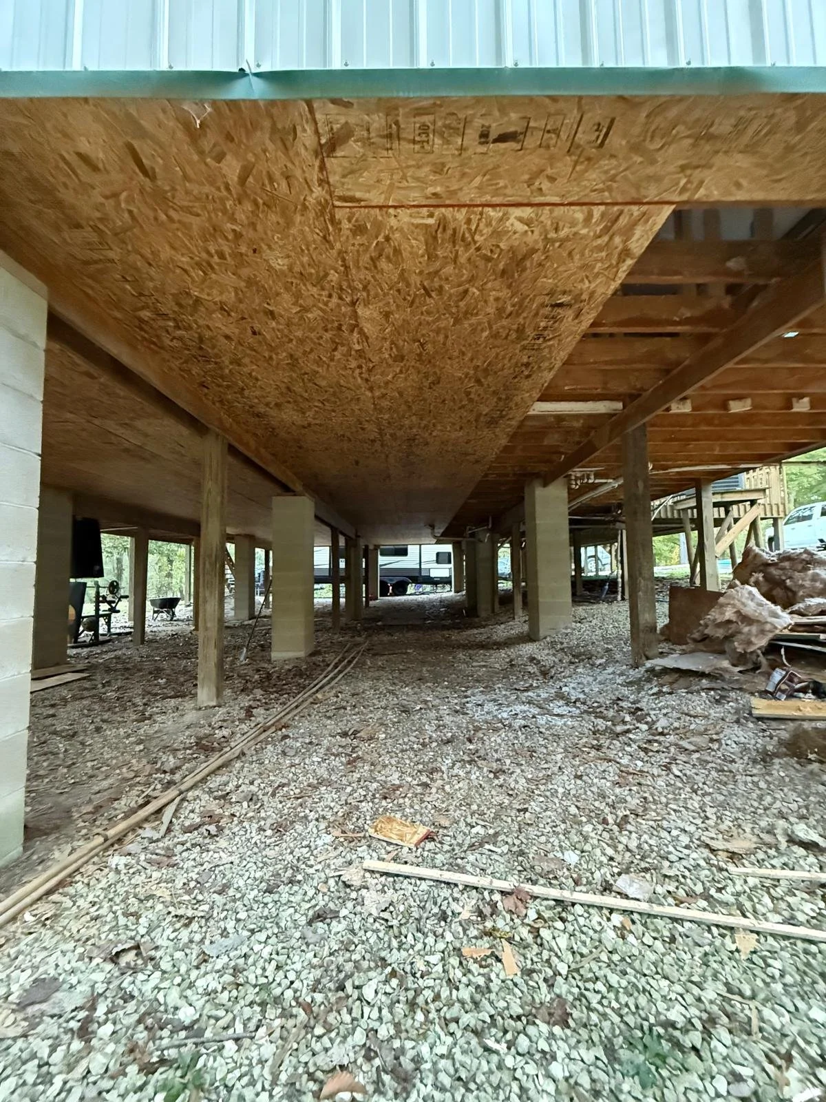 Exposed underside of a structure showing visible support columns, beams, and debris beneath the flooring system
