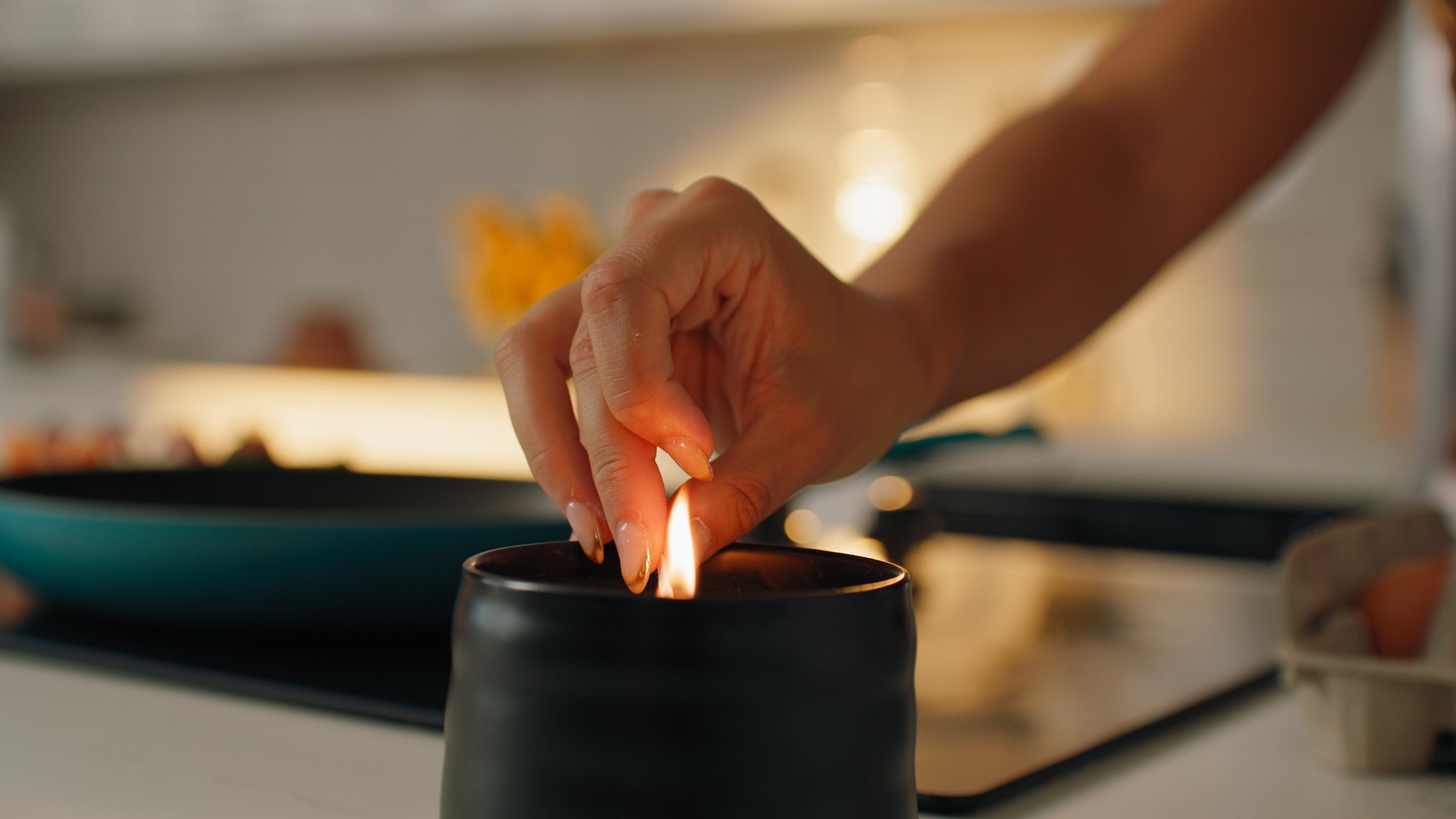 A person holding a lit candle over a black candle holder in a kitchen with a stove and blurred background