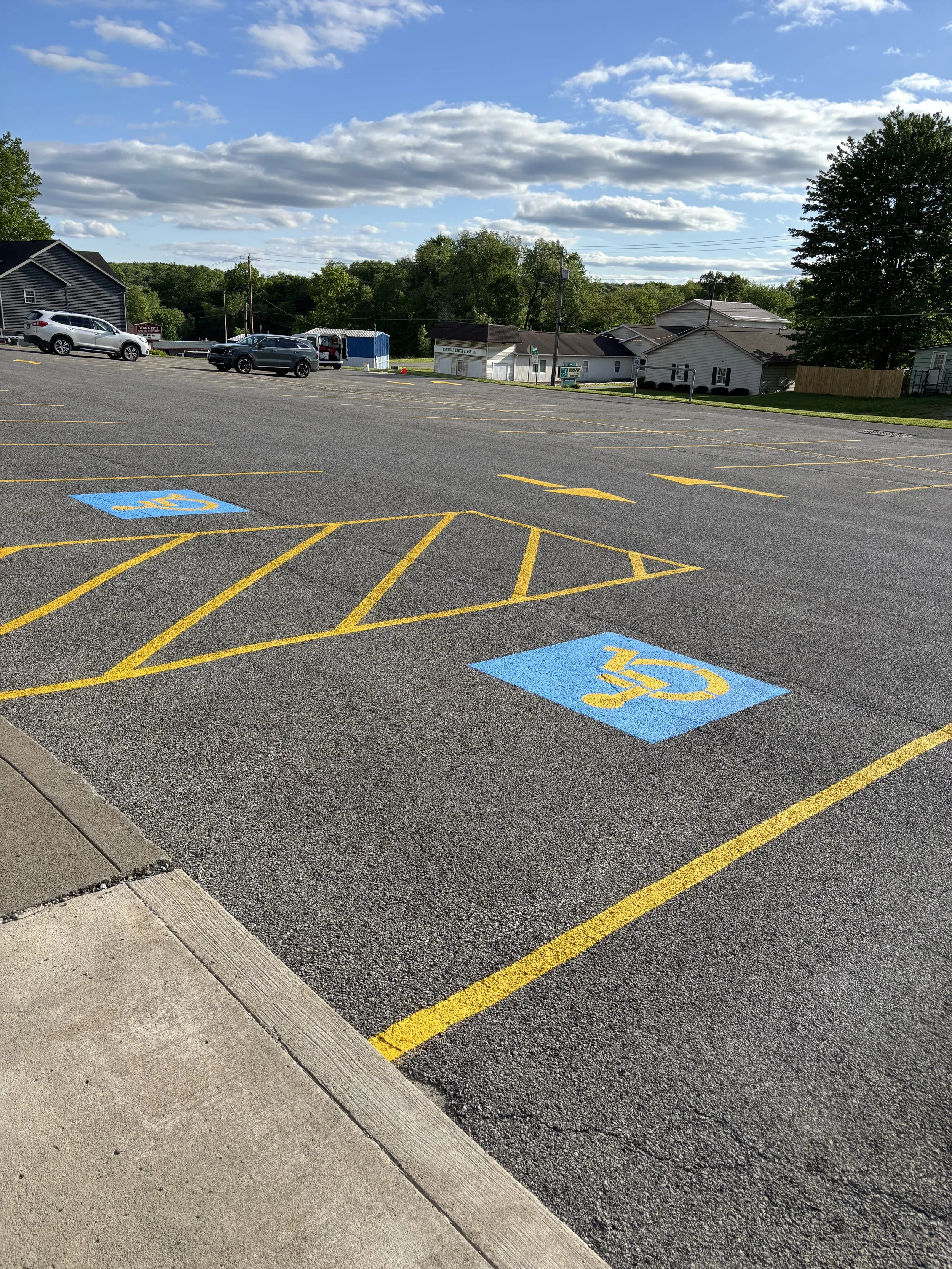Empty parking lot with designated handicapped parking spaces marked with blue and yellow symbols, under a partly cloudy sky.