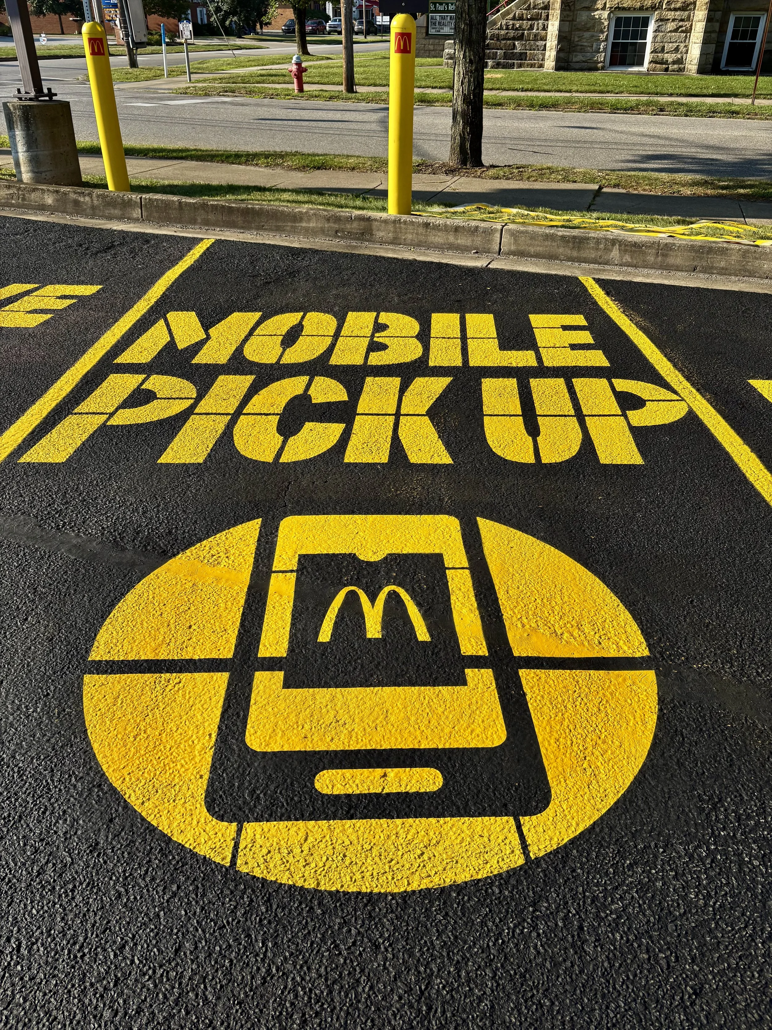 A parking space designated for mobile order McDonald's pickup with bright yellow graphic and text on black asphalt reading 'Mobile Pickup' and a phone icon with the McDonald's logo.