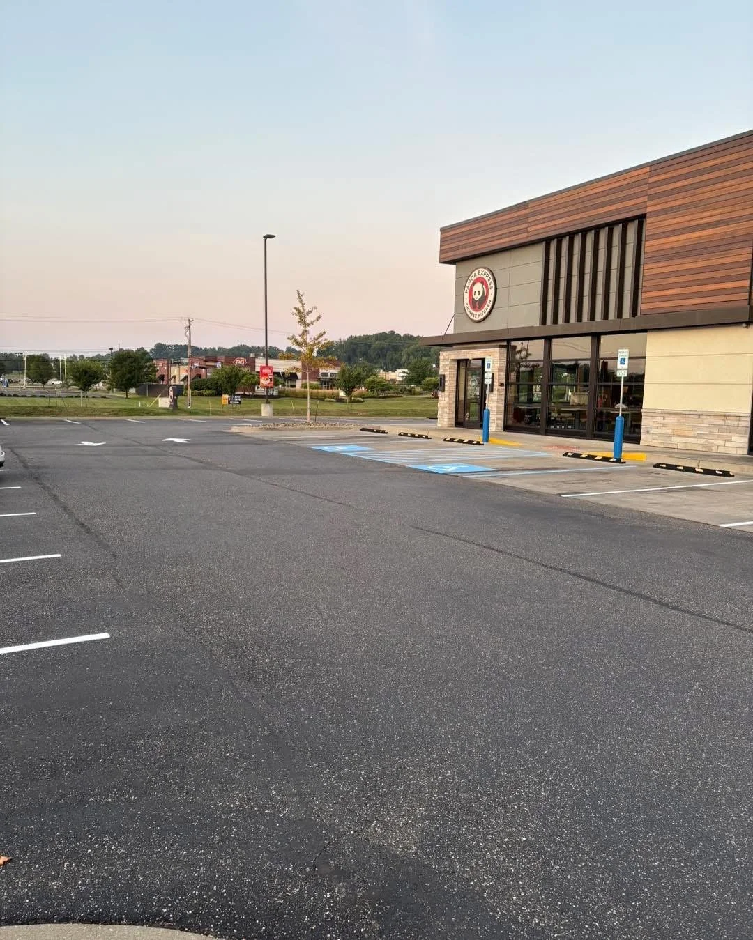 Empty parking lot outside a Panda Express restaurant with accessible parking spaces, a small tree, and a clear sky in the background.