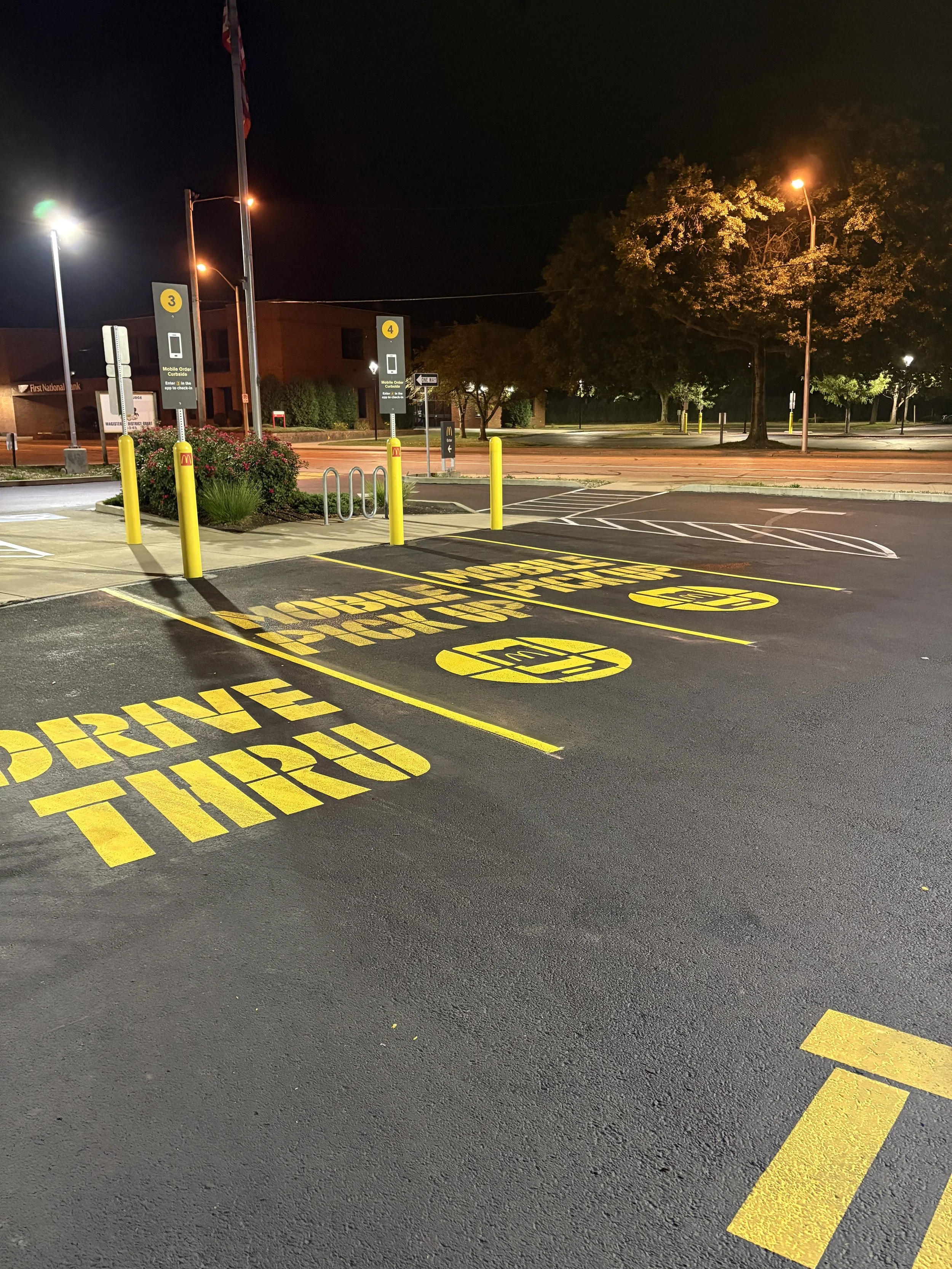 Empty drive-thru parking spaces at night with yellow painted instructions including 'DRIVE THRU' and signs for order stations numbered 3 and 4, illuminated by streetlights.