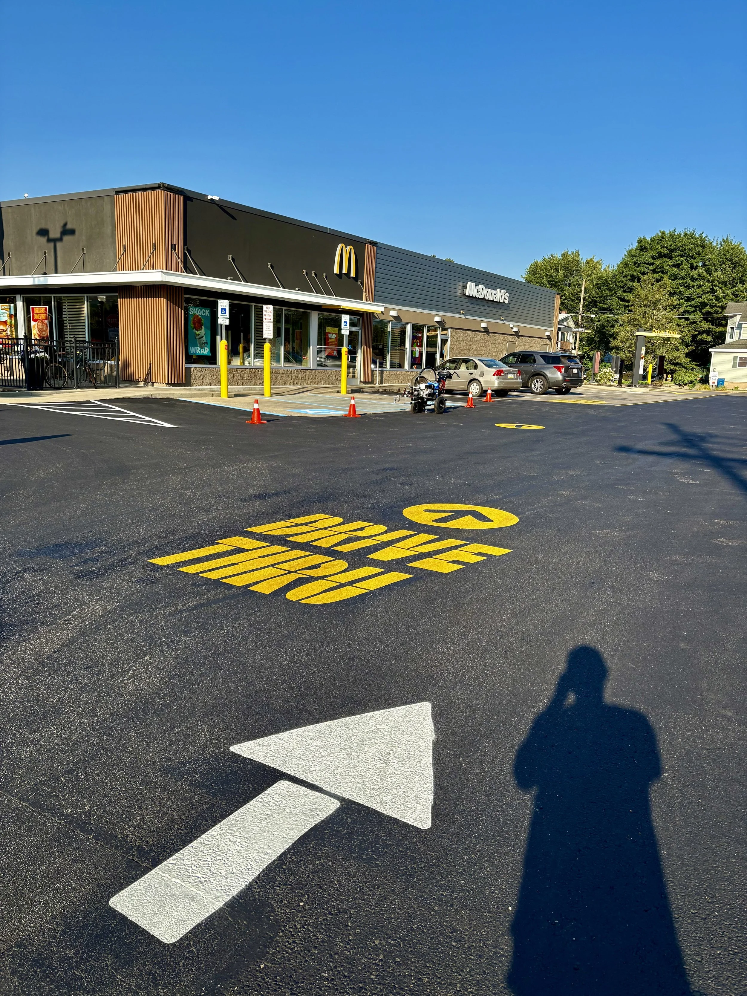 McDonald's restaurant with a parking lot, yellow 'Drive Thru' text painted on the asphalt, white arrow pointing forward, and several parked cars.