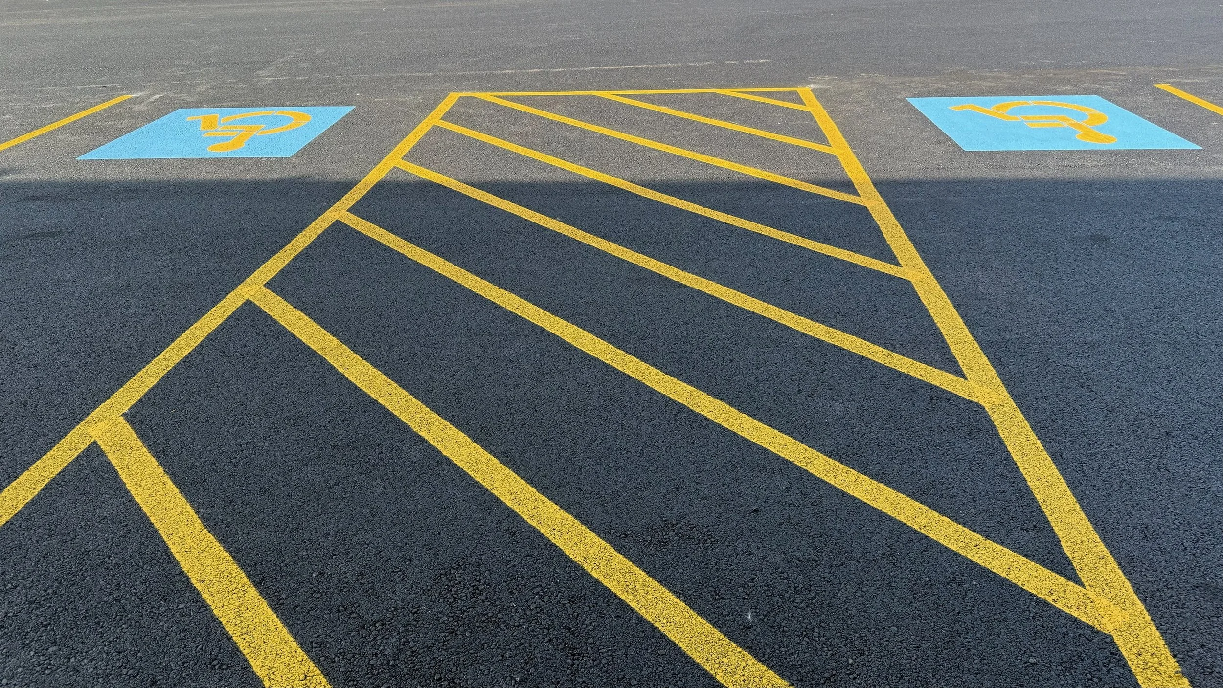 Parking lot with a designated handicapped parking space marked by blue square with yellow wheelchair symbol, no cars present.