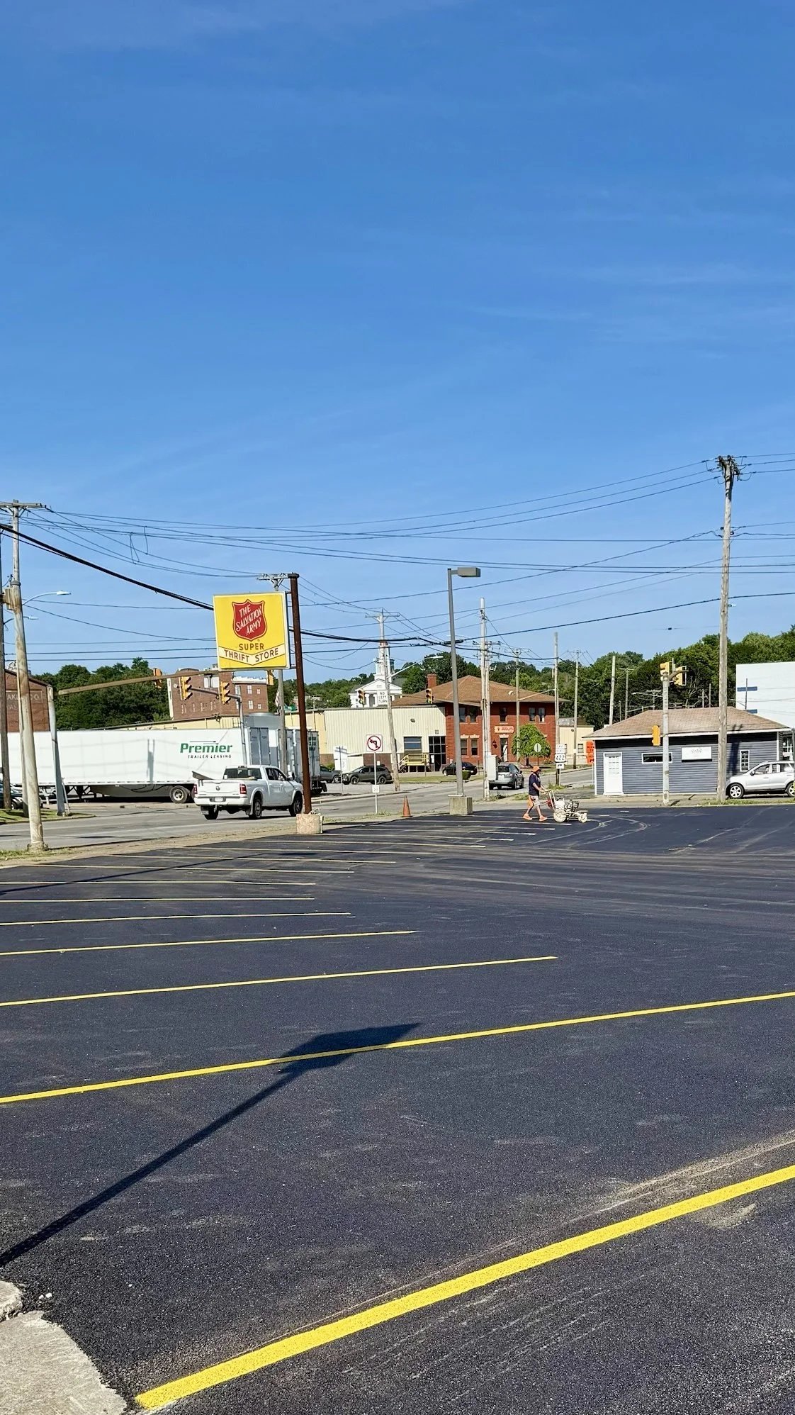 Empty parking lot in front of a small shopping strip with a sign for The Salvation Army Thrift Store, and a person pushing a shopping cart.