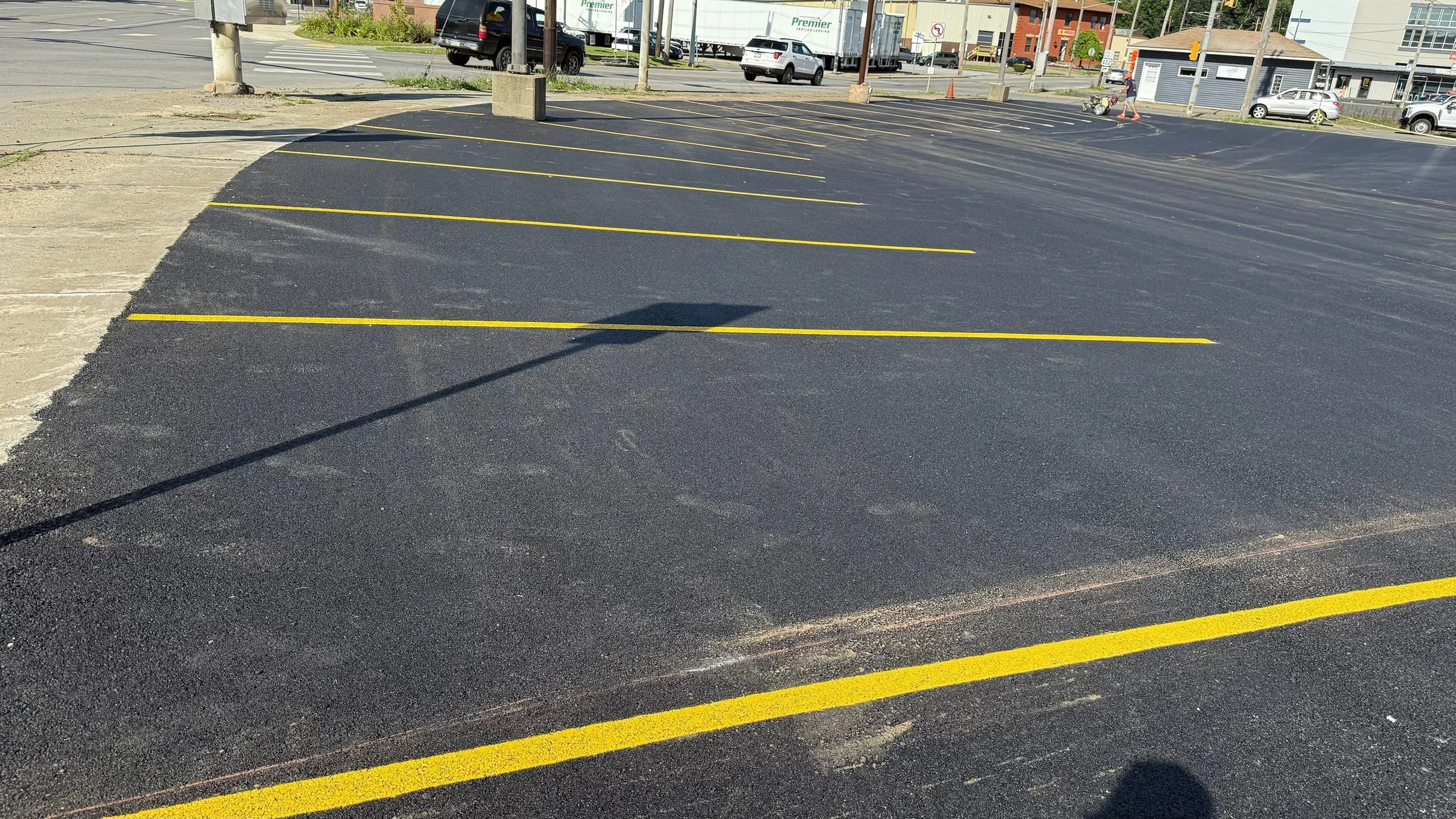 Empty parking lot with newly painted yellow parking lines, some cars and buildings in the background.
