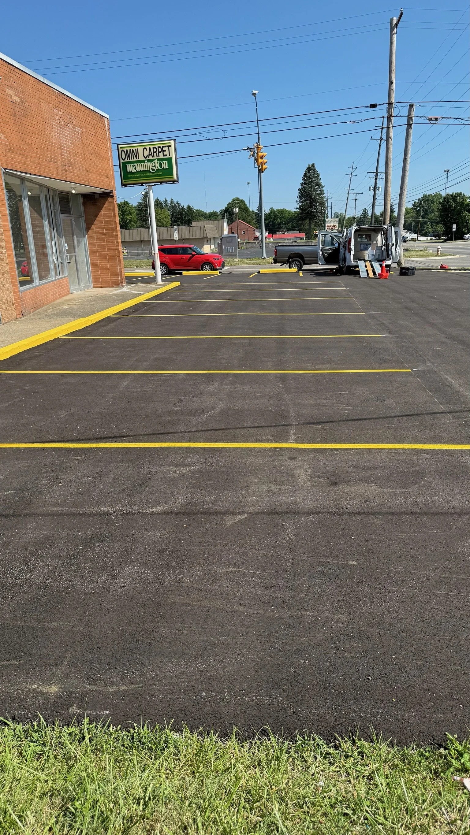 Empty parking lot outside a business with newly painted yellow parking lines, a brick building on the left, and a utility work van with equipment on the right.