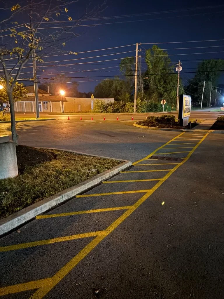 Empty parking lot at night with yellow striped parking spaces, a tree, power lines, and a billboard.