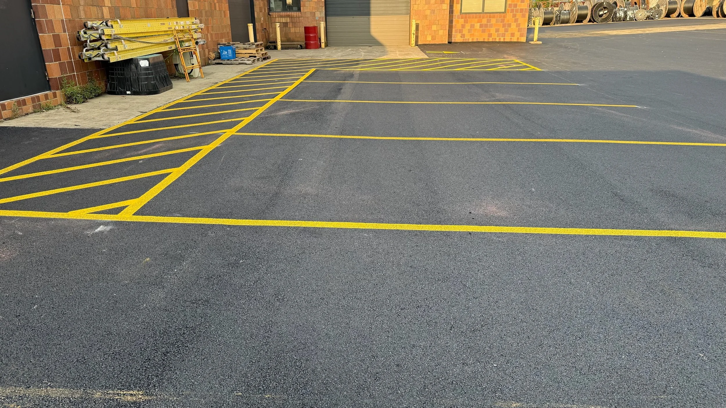 Empty parking lot with yellow-striped reserved parking spaces near a brick building, some stored equipment, and a closed garage door.