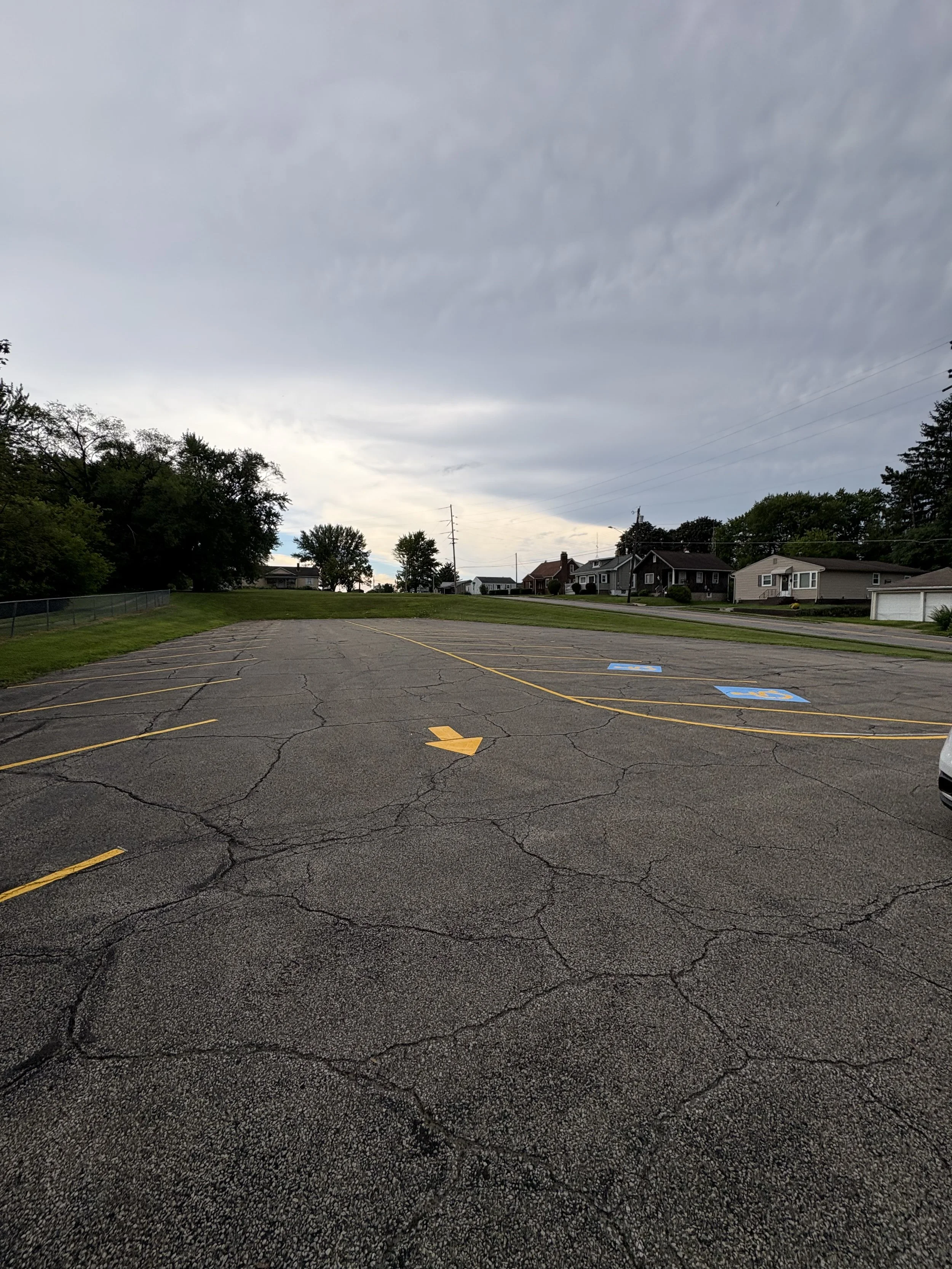 Empty parking lot with cracked asphalt, yellow directional arrow, and blue handicapped parking spaces, under a cloudy sky.