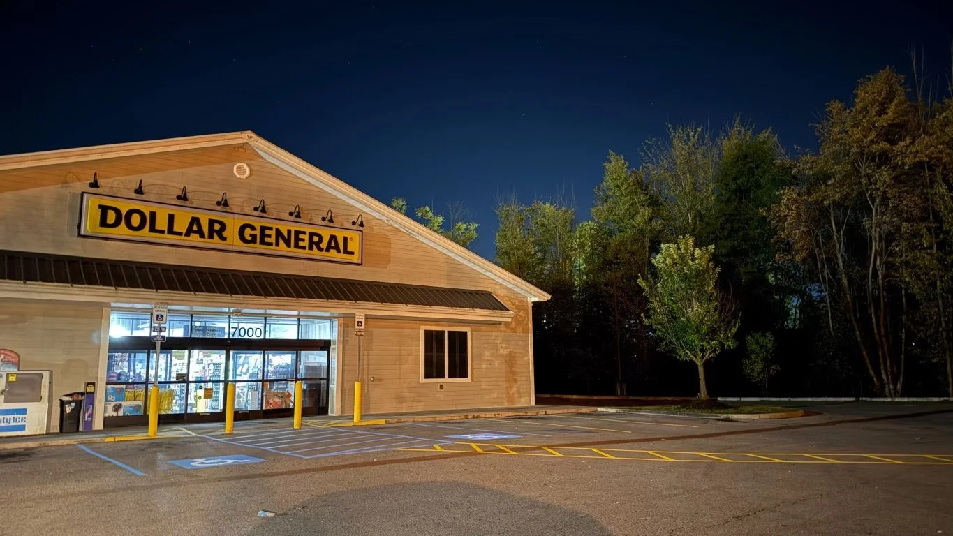 Empty parking lot in front of a Dollar General store at night, with trees in the background.