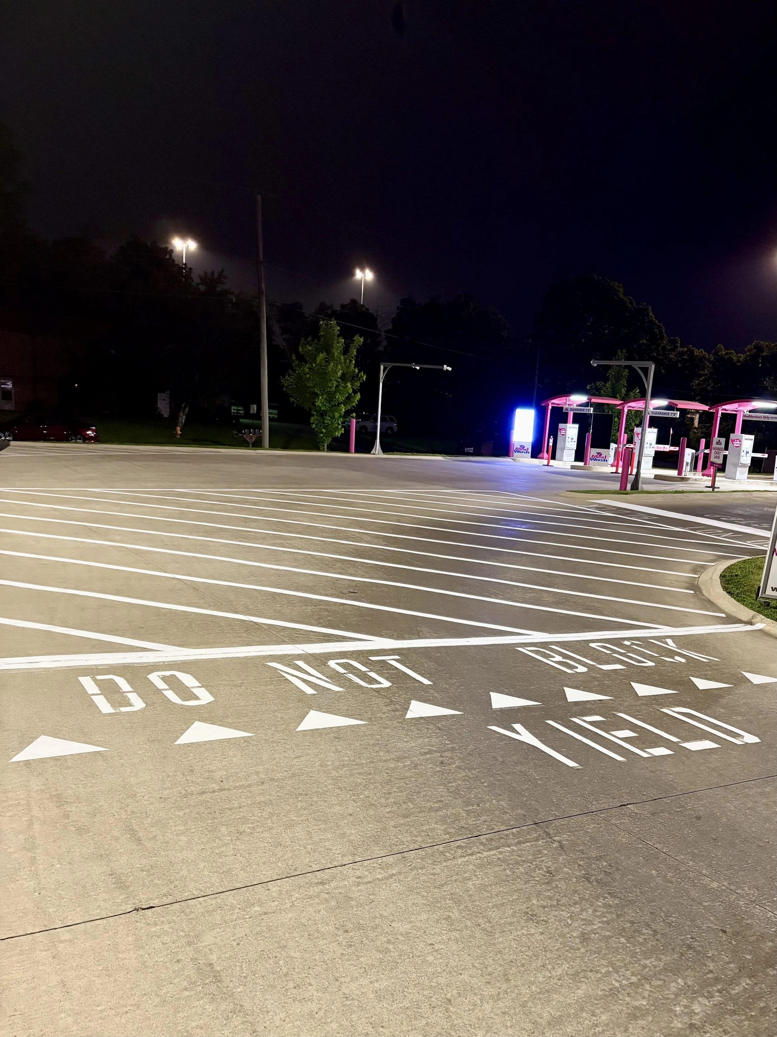 Empty parking lot at night with a message painted on the ground that says 'DO NOT BLOCK VIEW' and a brightly lit gas station in the background.
