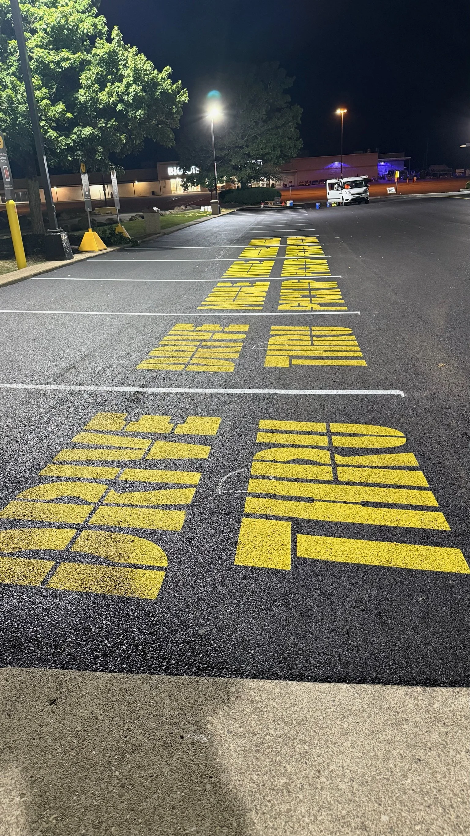 Nighttime view of a parking lot with yellow painted message on the ground reading, 'THANK YOU FRONTLINE WORKERS', illuminated by streetlights.