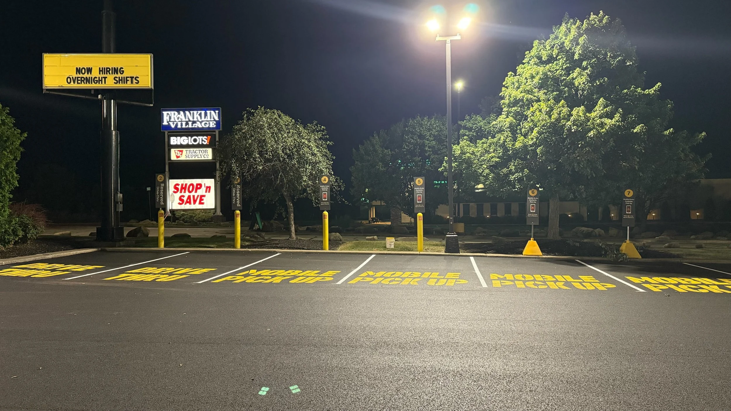 Empty parking lot at night with designated handicap spots and a large sign advertising jobs at Franklin Village.