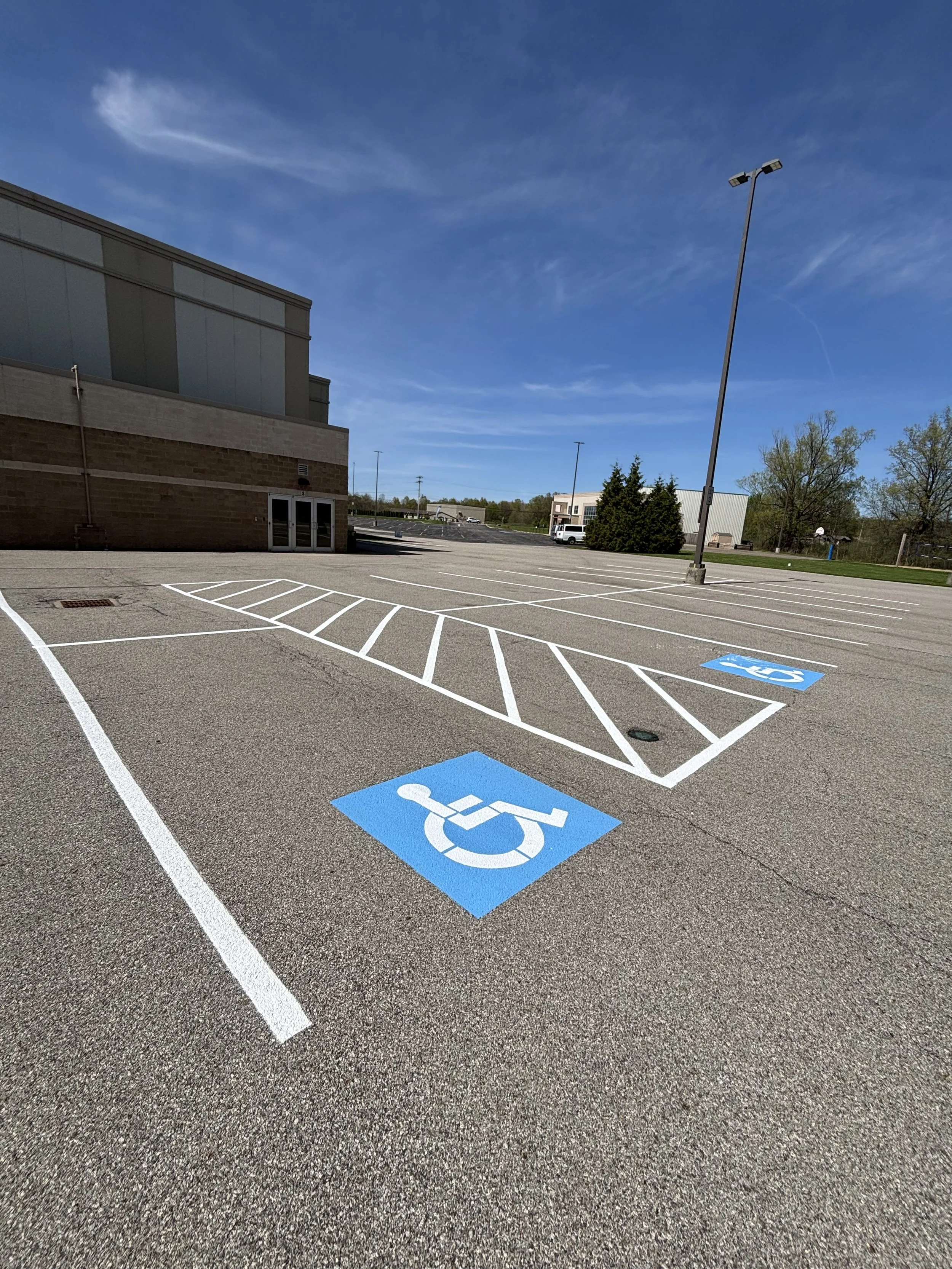 Empty parking lot with handicap symbols painted in blue and white, leading to a building under a clear blue sky.