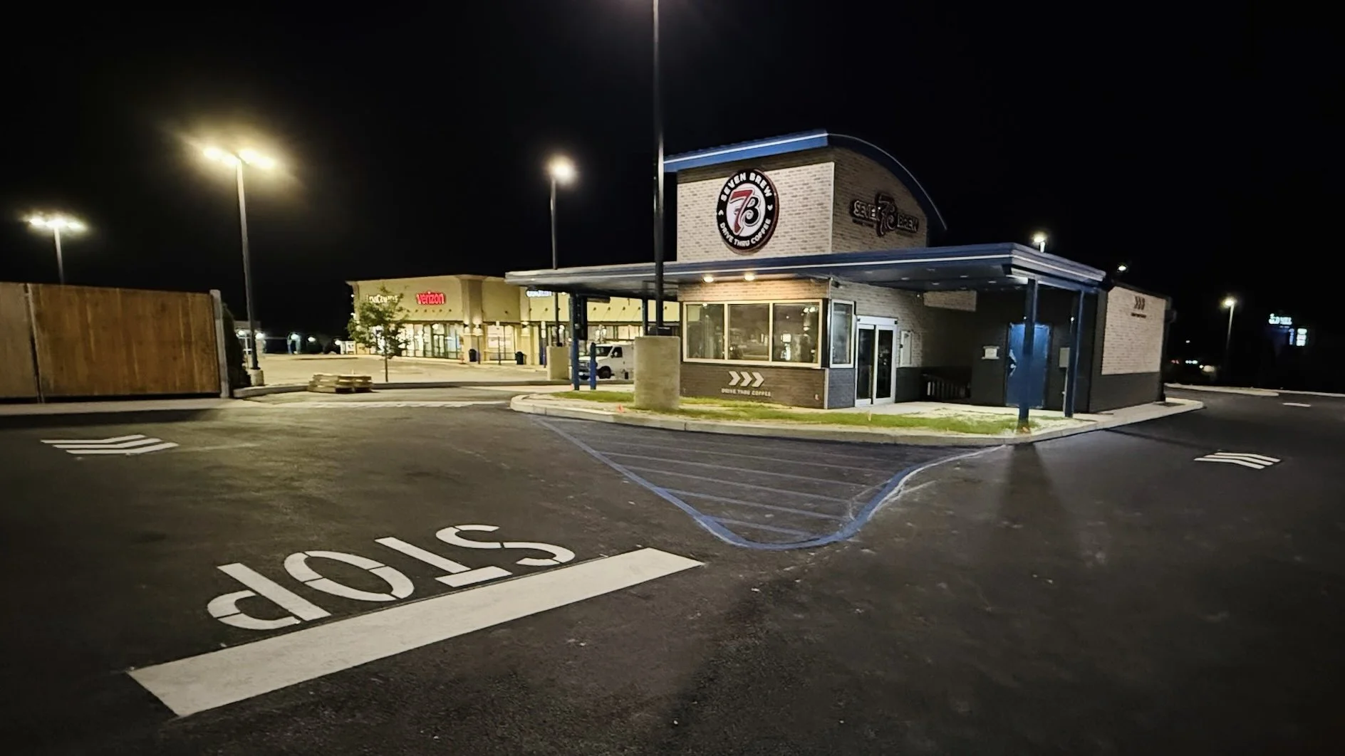 Nighttime view of a fast food restaurant, Shake Shack, with a parking lot and a stop sign marked on the pavement, illuminated by streetlights.