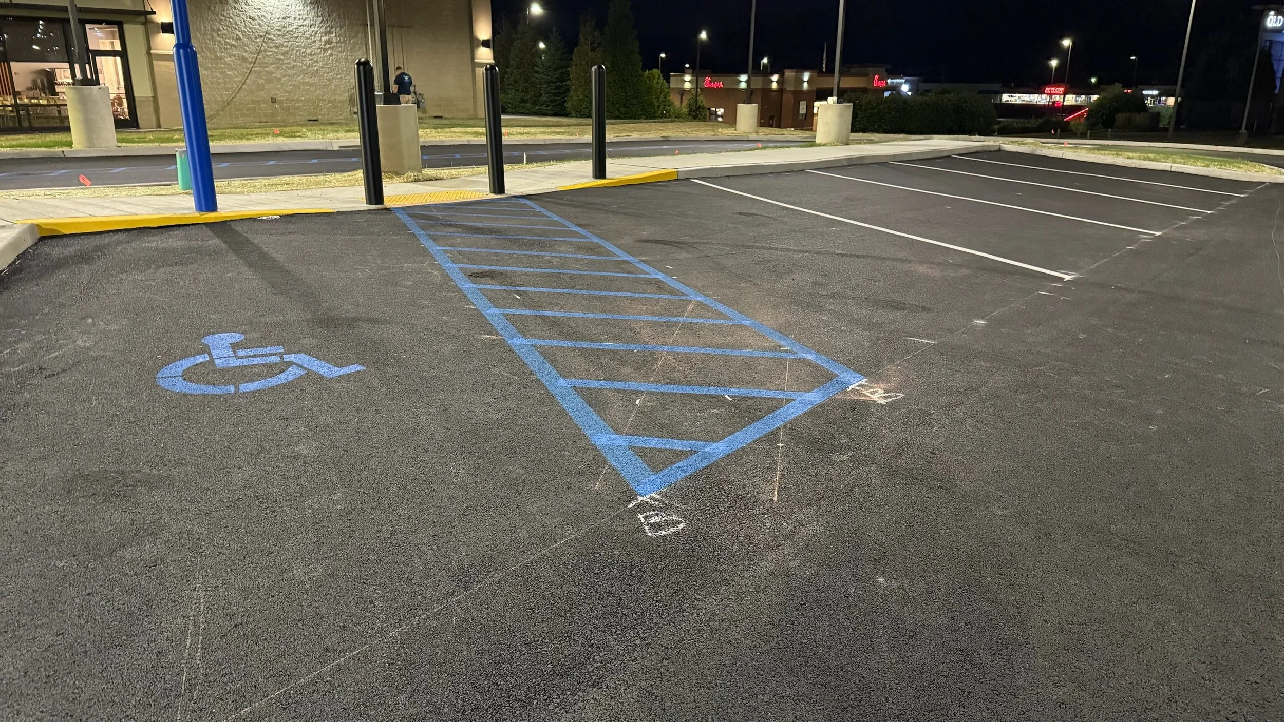 Empty parking lot with designated handicap parking space marked with blue lines and wheelchair symbol, near the entrance of a building at night.