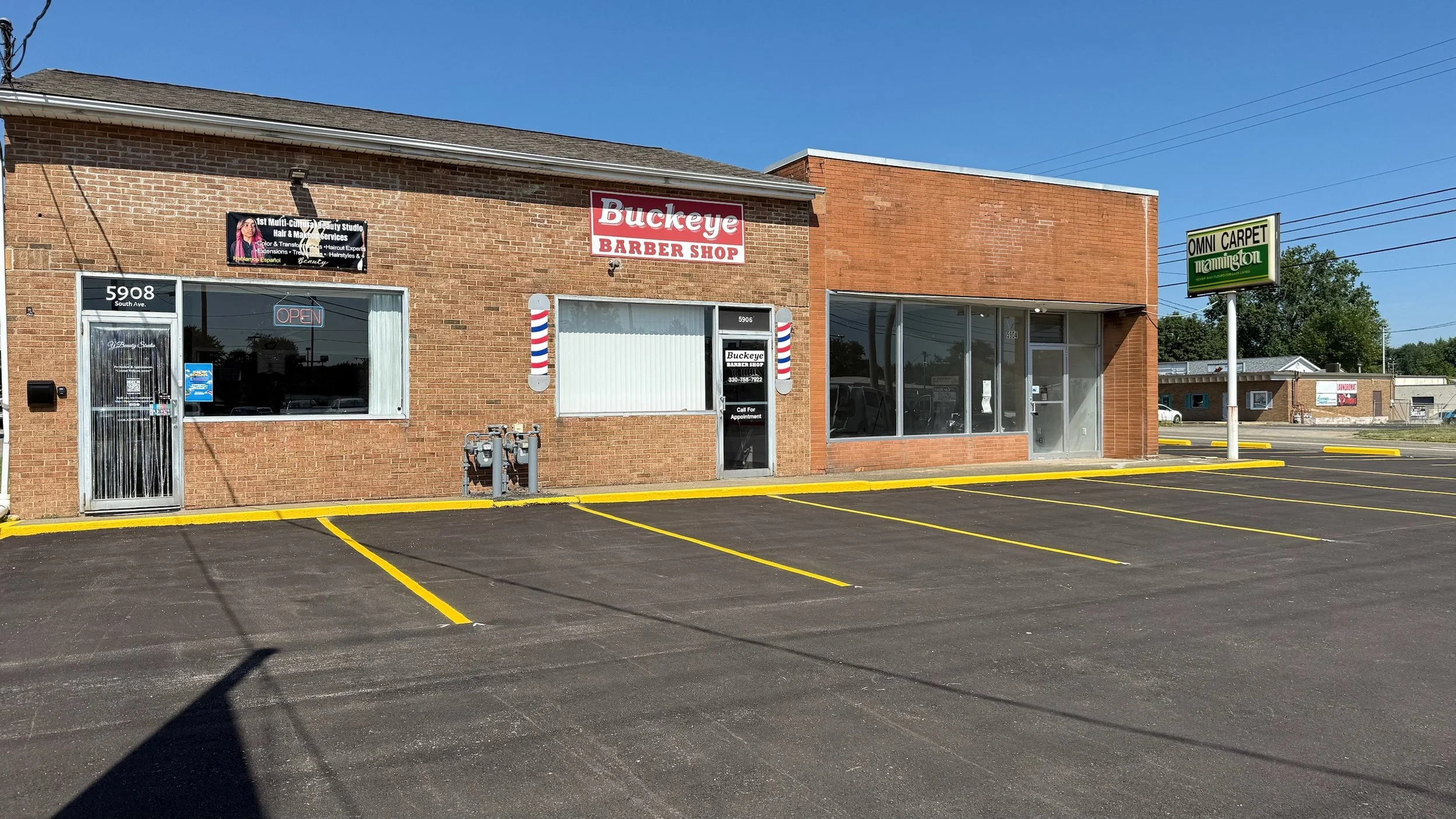 Brick building with a barber shop sign, barber pole decorations, and an empty parking lot with yellow lines.