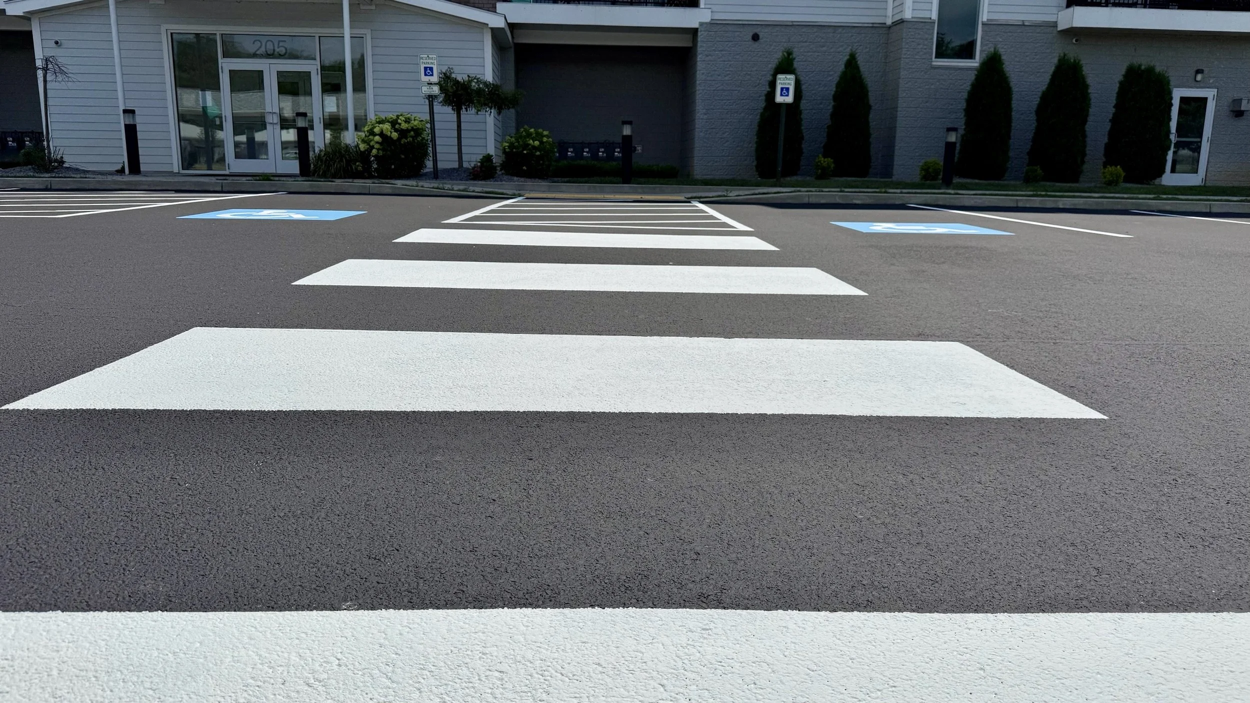 A pedestrian crosswalk with white stripes and two blue handicap parking spaces on a paved parking lot in front of a building.