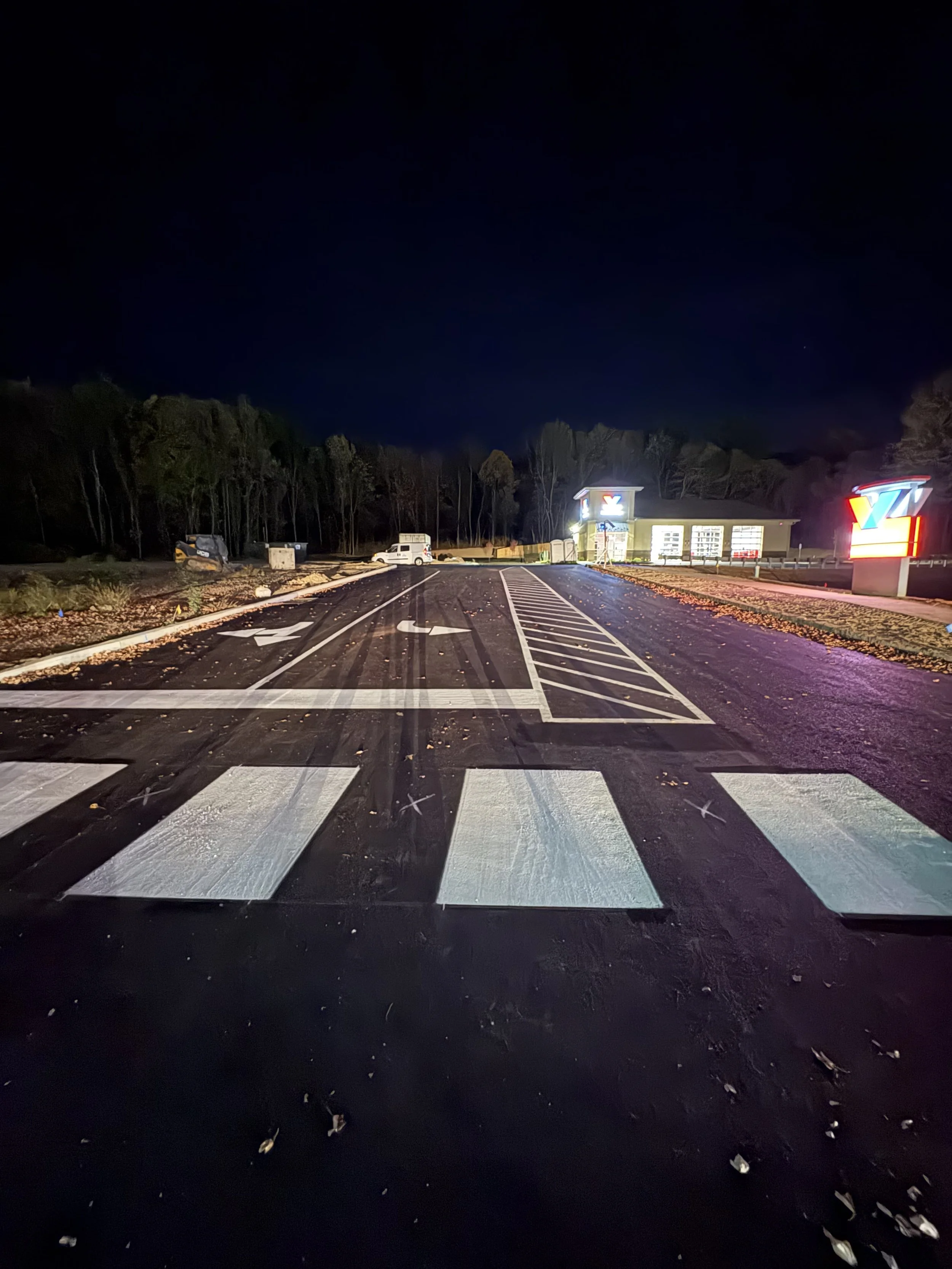 Nighttime view of an empty parking lot with a grocery store in the background, illuminated by bright lights and colorful store signage.