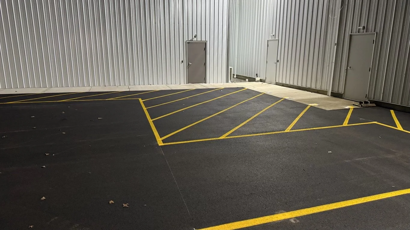 Empty parking lot with marked parking spaces outlined in yellow, adjacent to a metallic building wall with two doors.