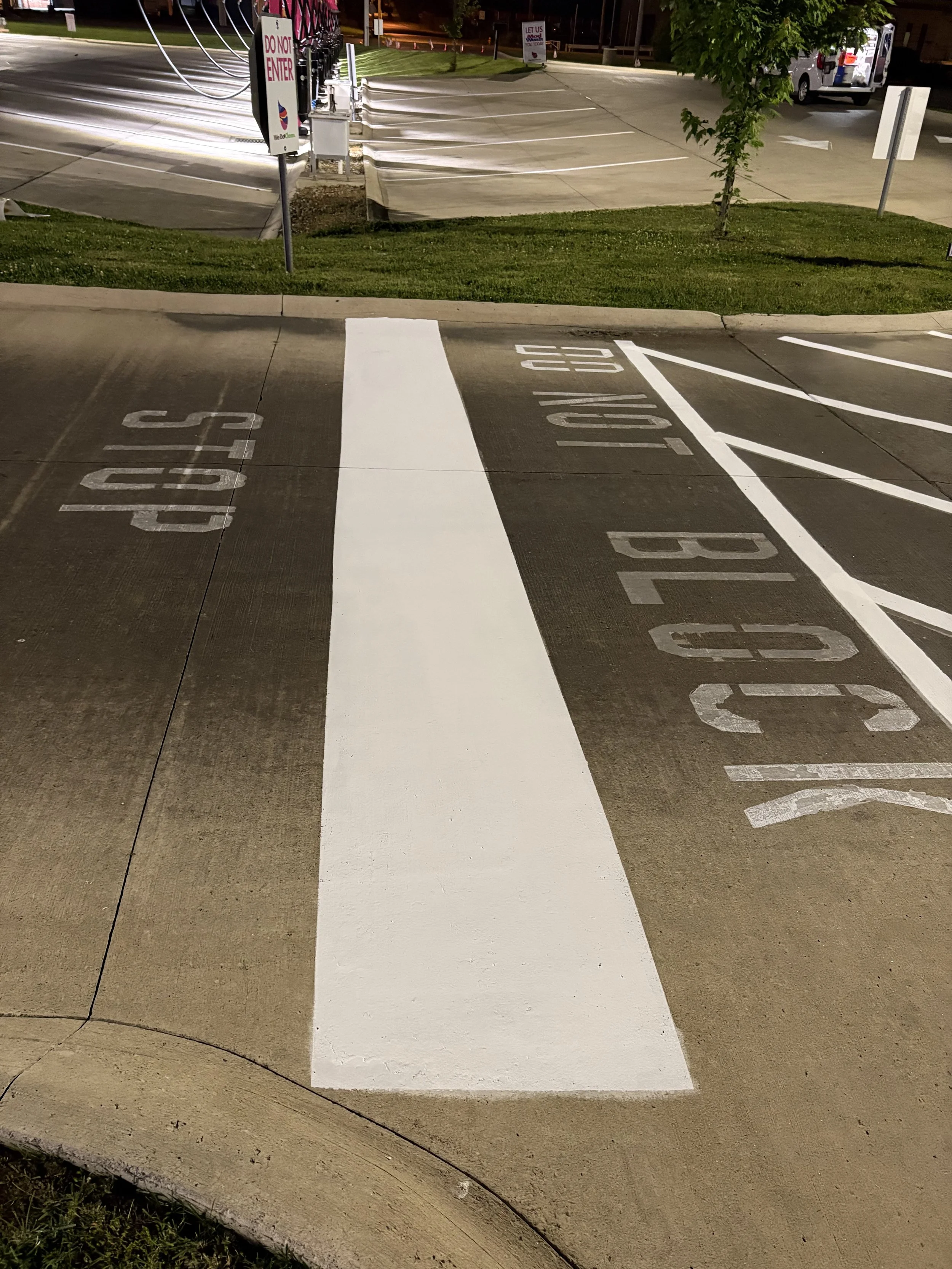 Nighttime image of a parking lot with a freshly painted white crosswalk and the words 'STOP' written on the pavement, and several parked vehicles in the background.