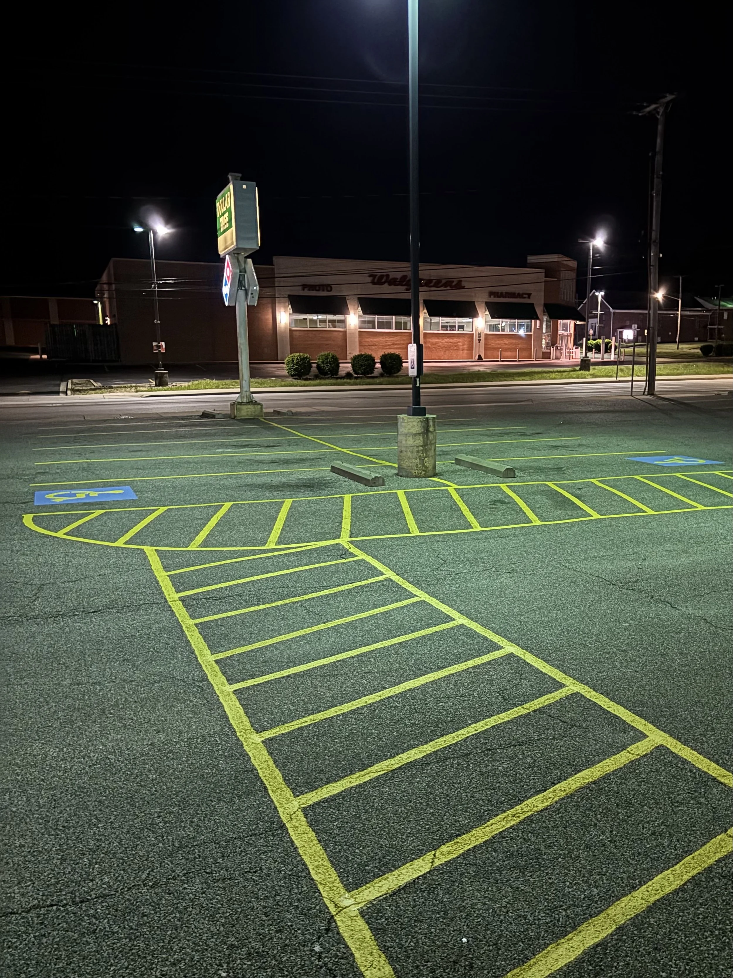 Empty parking lot with yellow painted handicap parking spaces and striped accessible path at night, Walgreens store in the background.