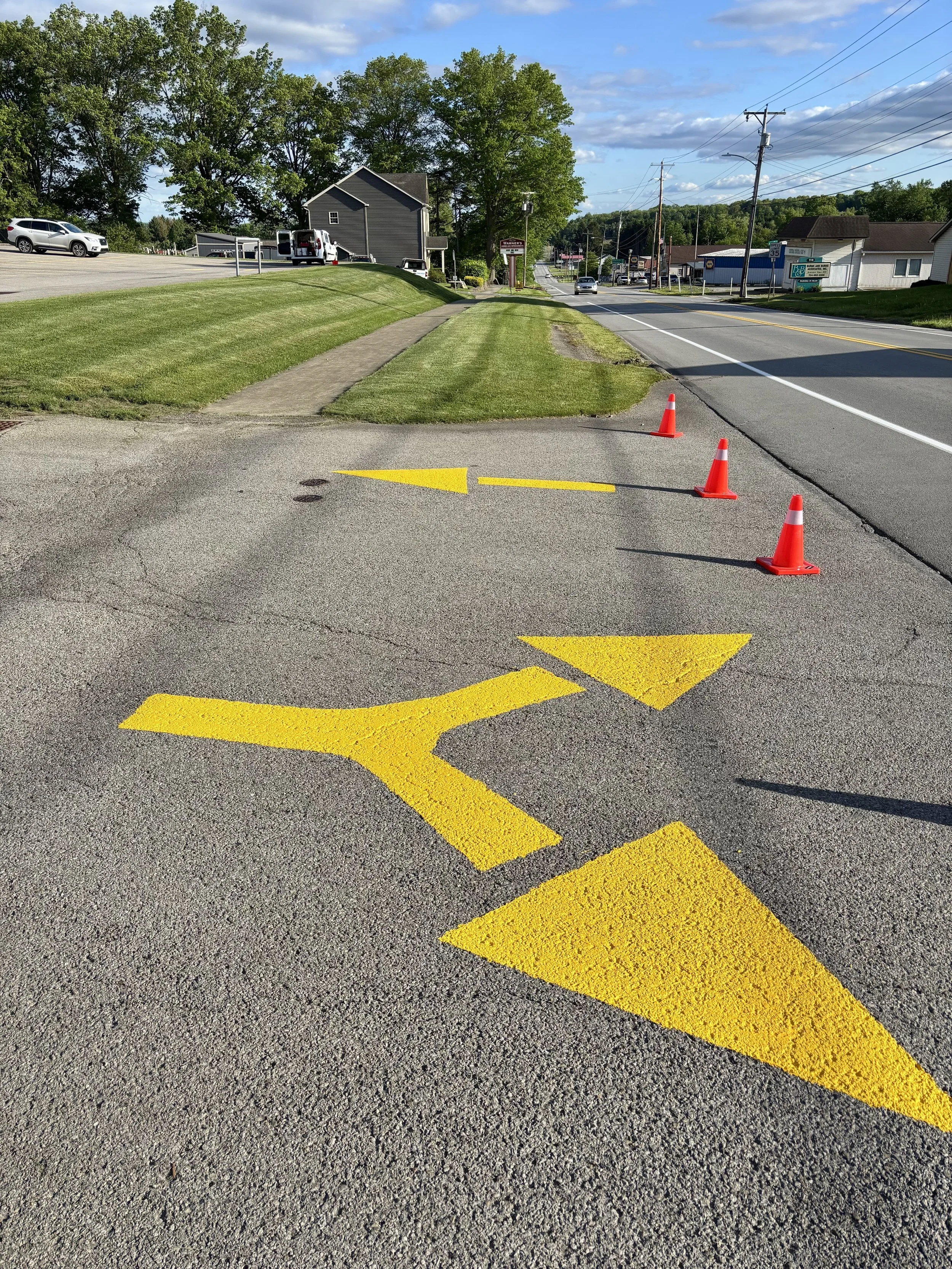 A parking lot with yellow directional arrows painted on the asphalt, blocked off by orange traffic cones.