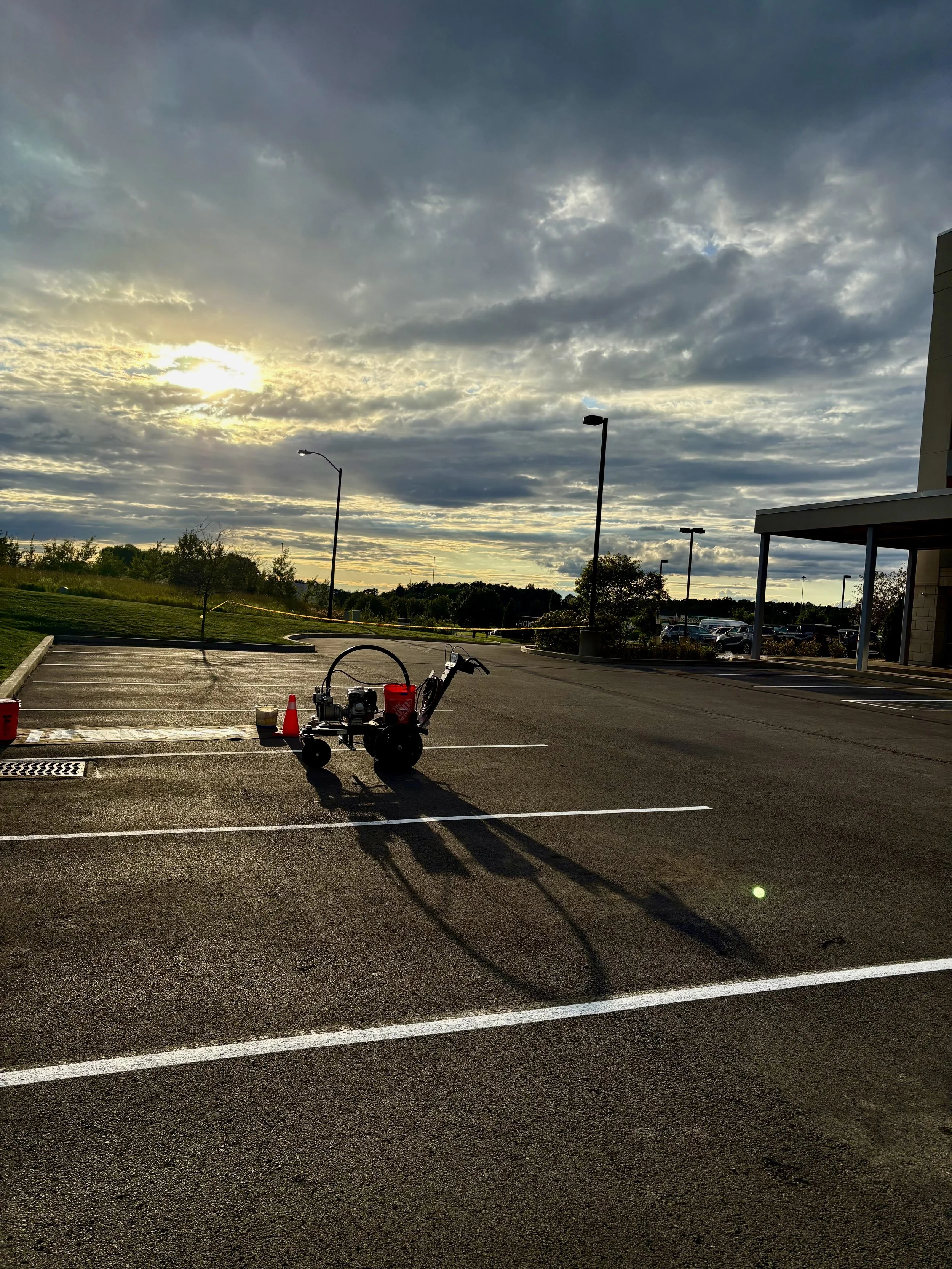 Empty parking lot with a pressure washer and orange cones, under a cloudy sunset sky.
