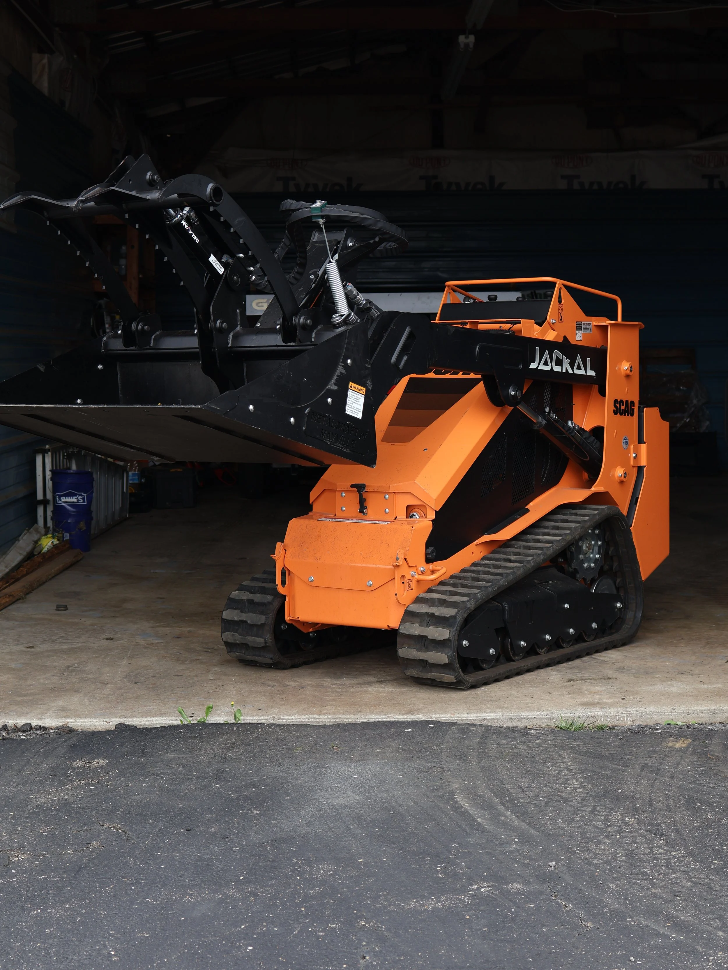 Orange tracked ASV skid steer with a black grapple bucket parked inside a garage