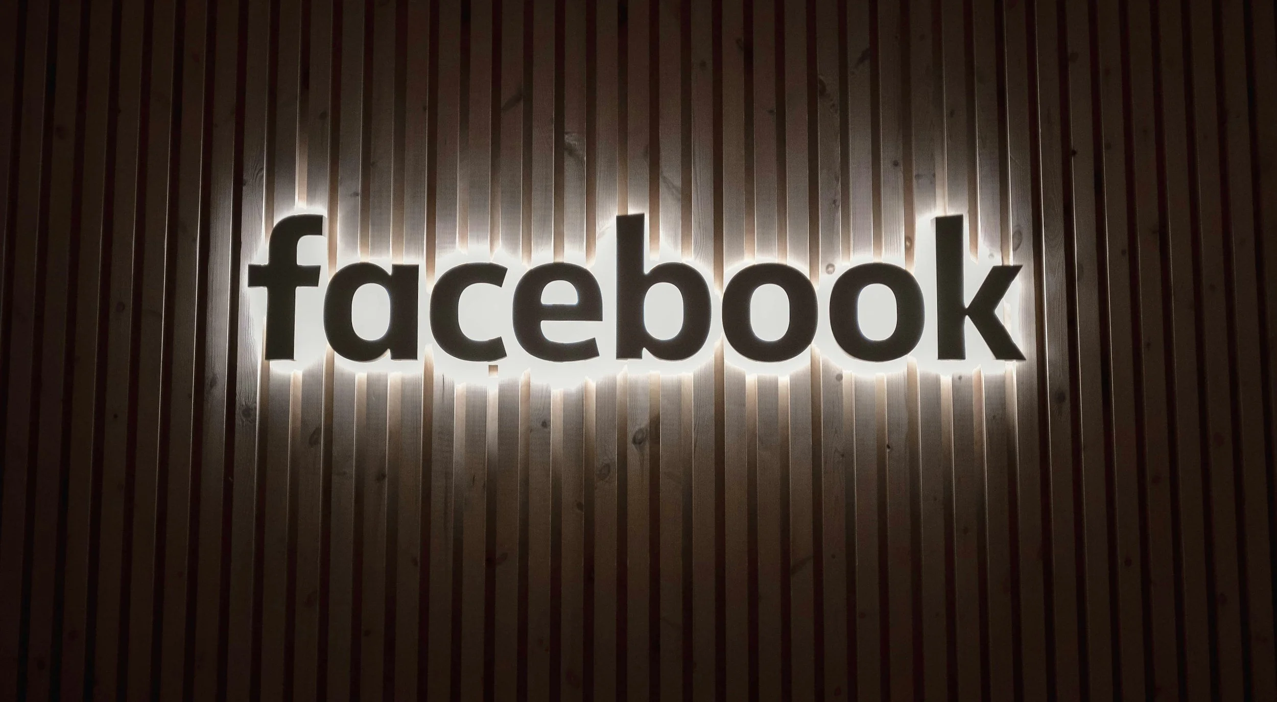Illuminated "facebook" sign on a wood textured background.