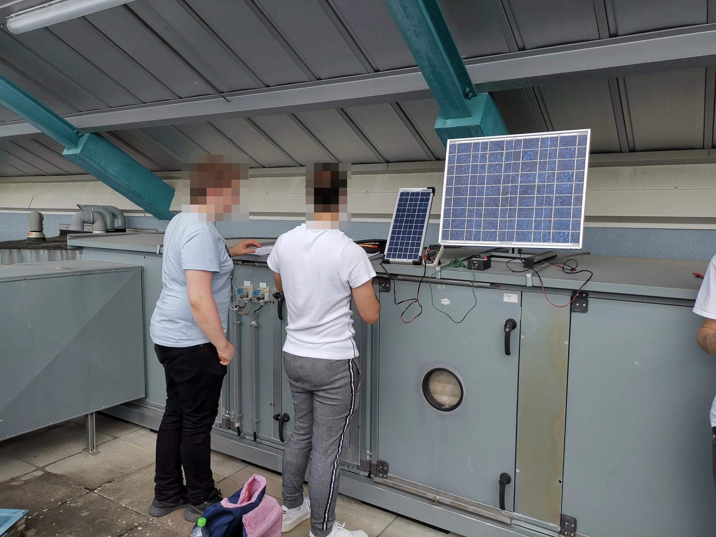 Menschen arbeiten an einer technischen Anlage mit Solarmodulen unter einer Dachkonstruktion.