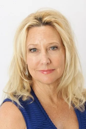 A blonde woman with shoulder-length hair, wearing a blue top, looking directly at the camera with a slight smile, against a plain white background.