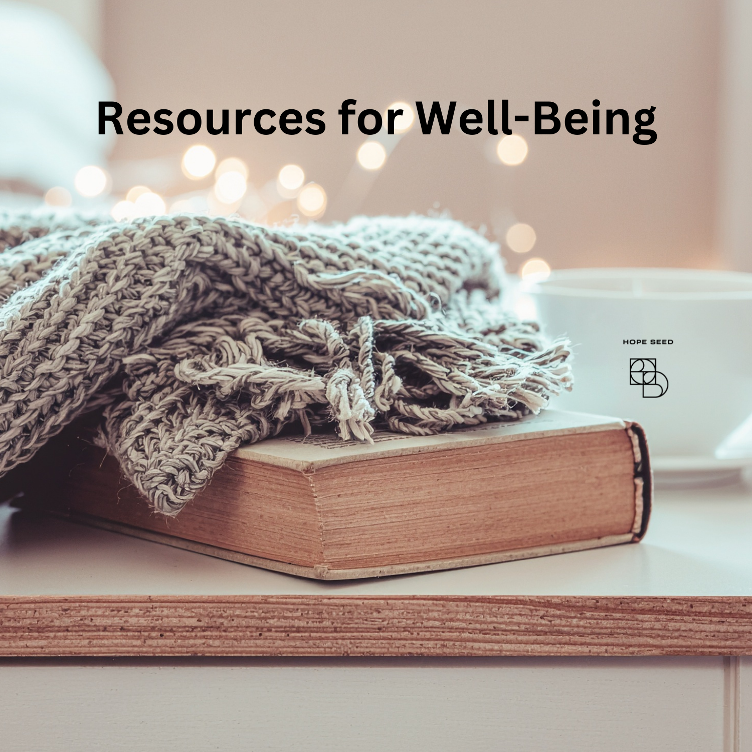 A cozy scene with a hardcover book, a knitted gray throw blanket, and a coffee mug with the Hope Seed logo, on a white surface with warm, blurred string lights in the background. The text "Resources for Well-Being" is overlaid on the image.