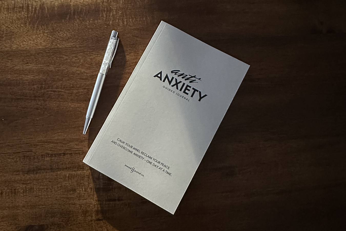 A guided journal titled 'anti anxiety' with a silver pen placed beside it on a wooden surface.