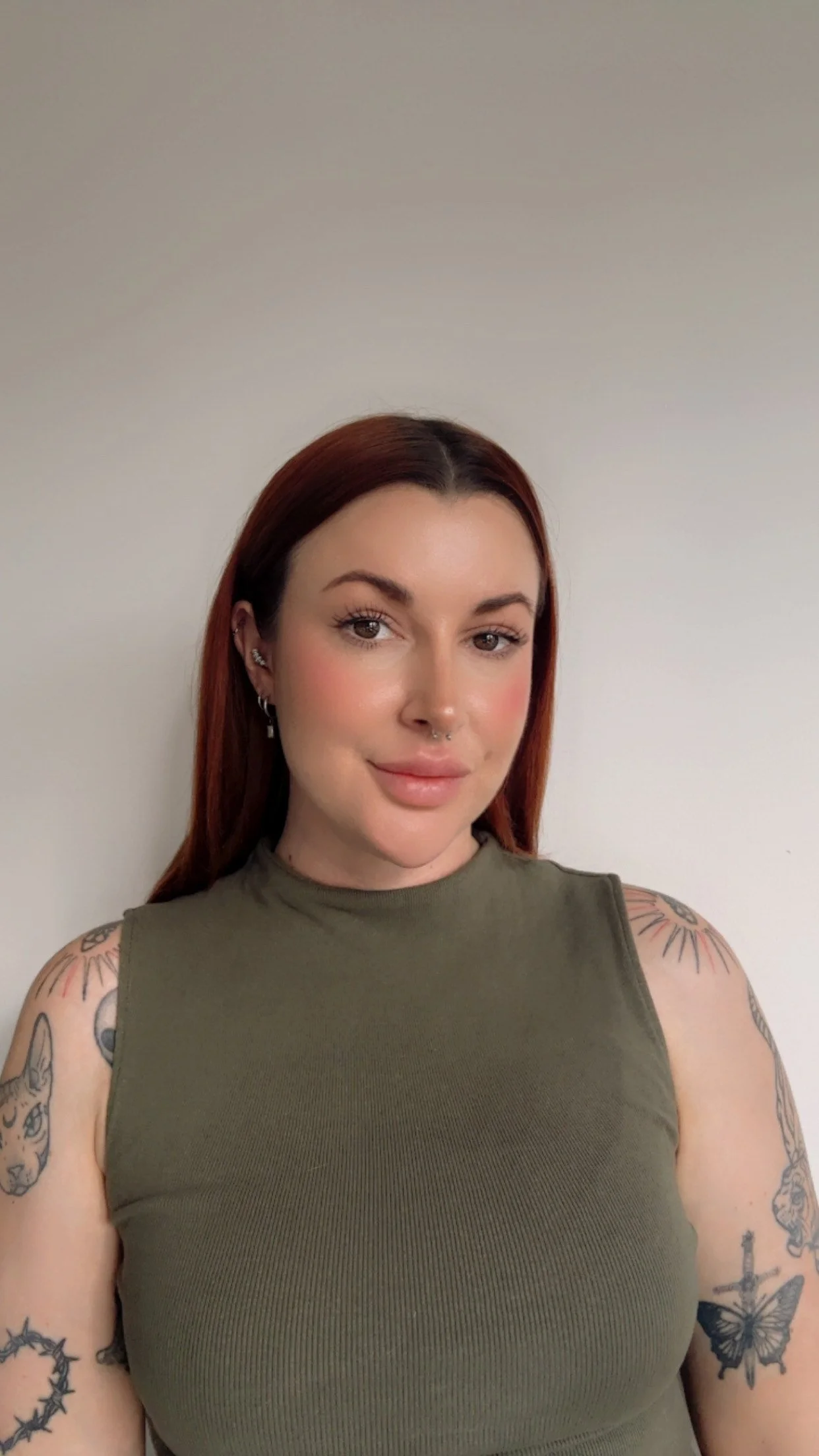 A photo of Tamara, the owner of inward journal co with copper hair, wearing a sleeveless olive green top, standing against a plain wall.