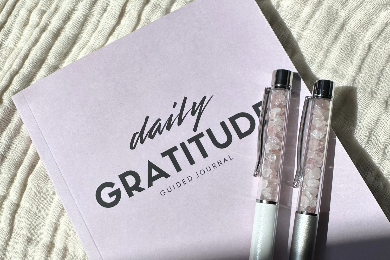 the daily gratitude journal by inward journal co lying on a textured cloth background with crystal healing pens