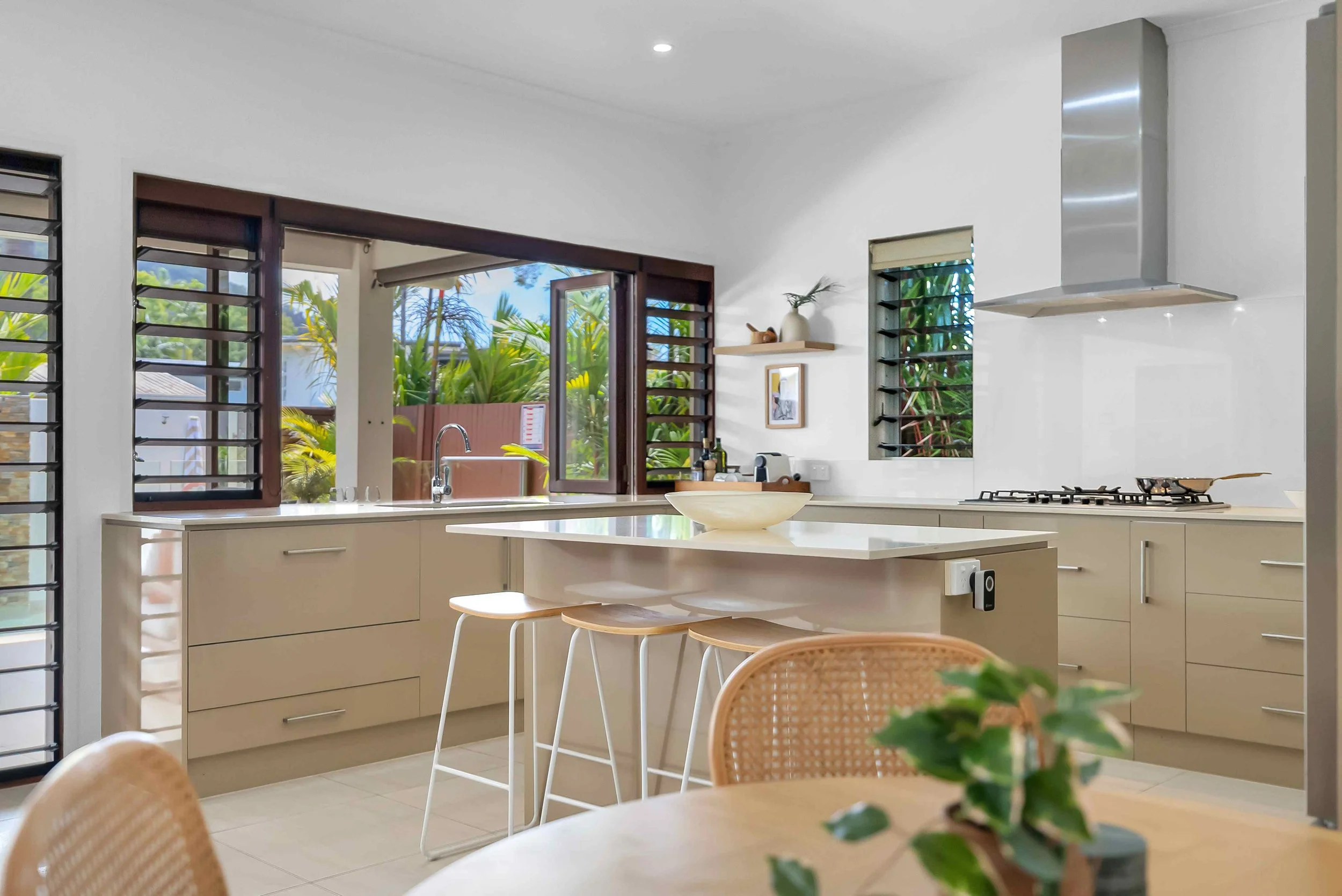 Modern kitchen with beige cabinets, island with barstools, stainless steel appliances, and large window.
