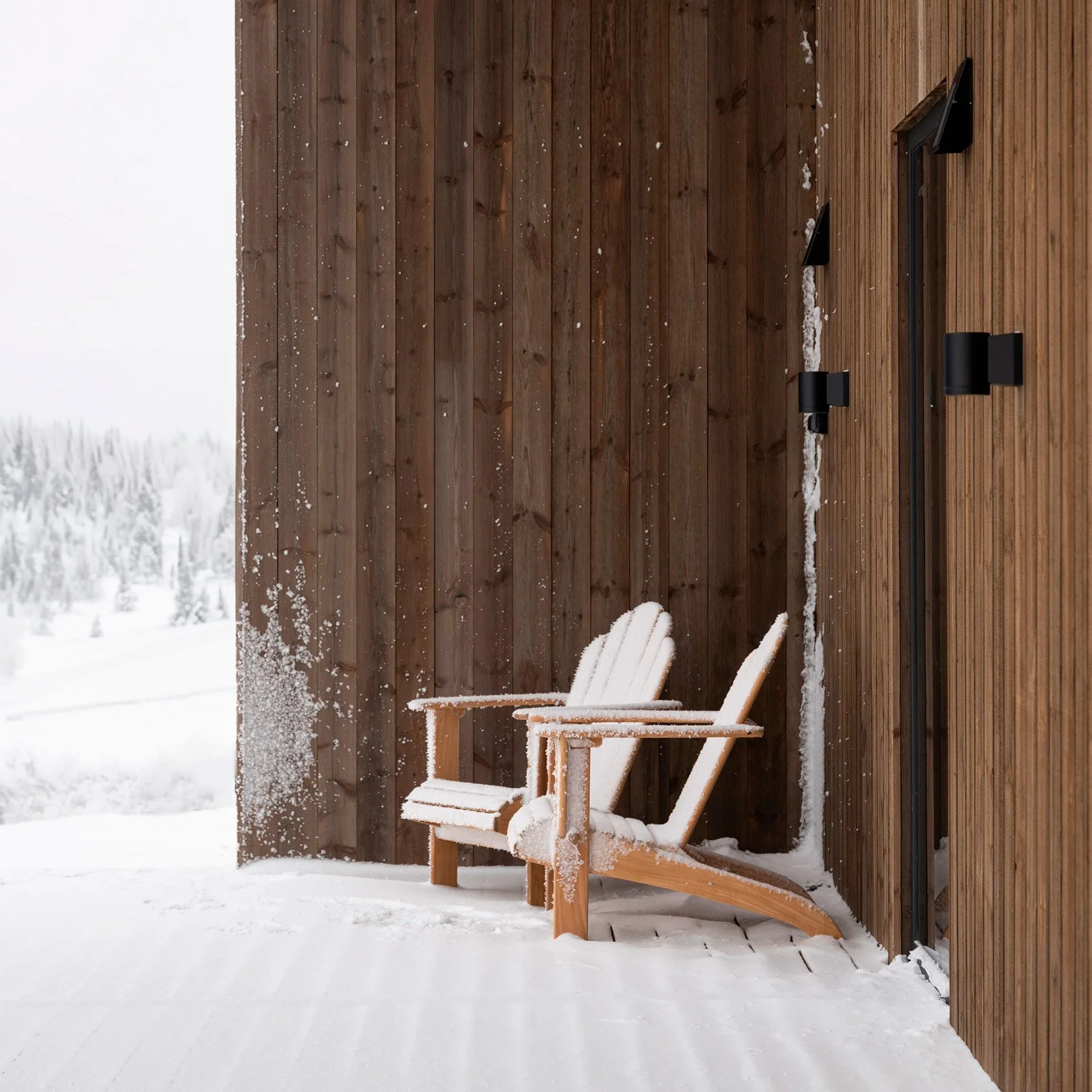 To trestoler på en terrasse med snø. Snødekt landskap i bakgrunnen, vertikalt trepanel på veggen.