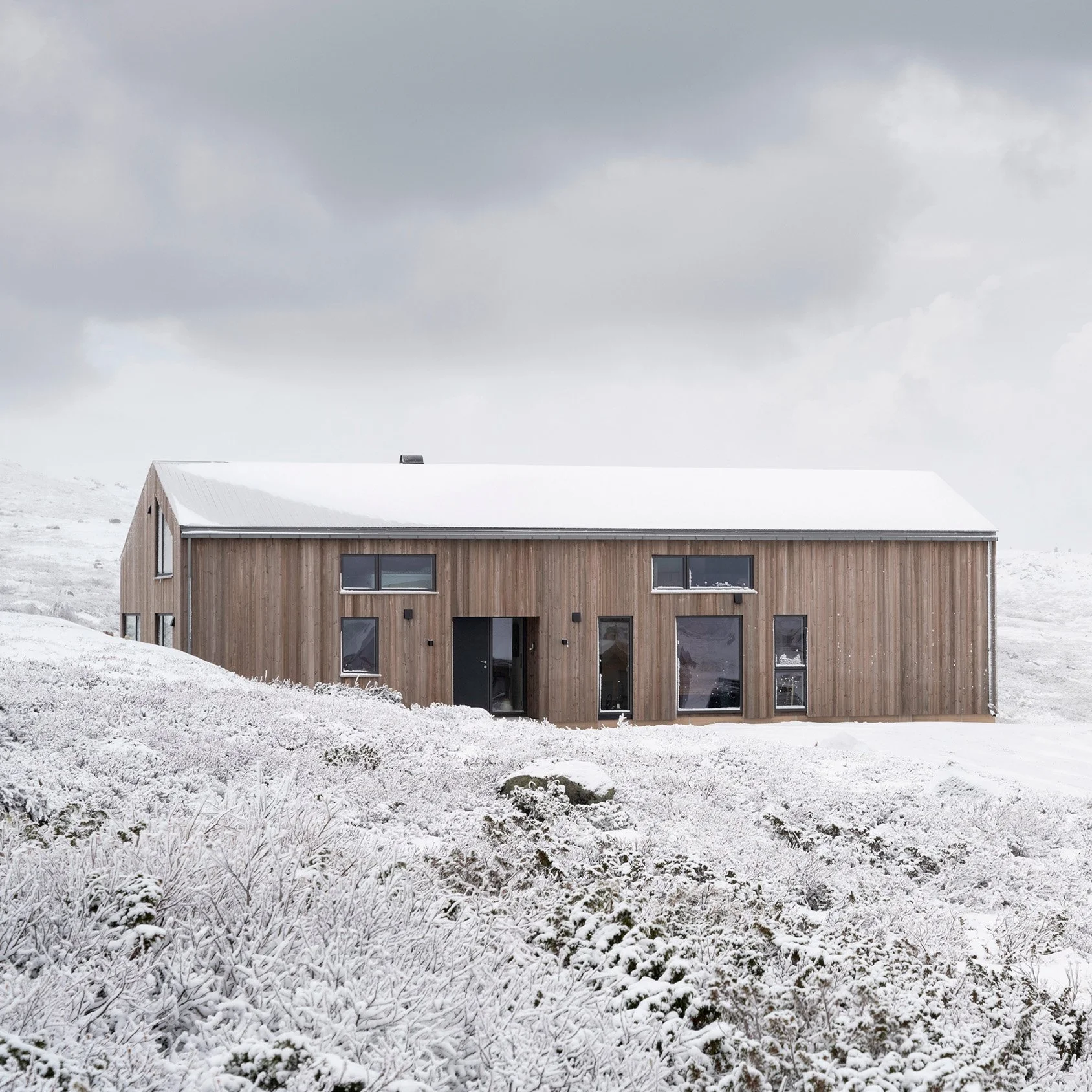 Utvendig bilde av Sikt-hytte, omgitt av snødekt landskap under en overskyet himmel.