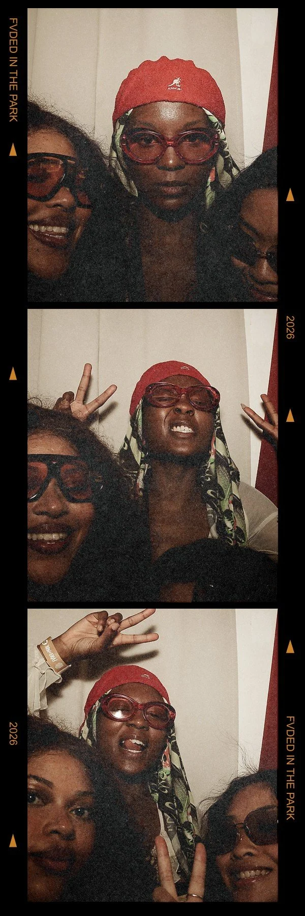 Three women in a photo booth making different gestures. The woman in the middle wears red glasses, a red headscarf, and a patterned scarf. The woman on the left wears glasses and is smiling, and the woman on the right is only partially visible.